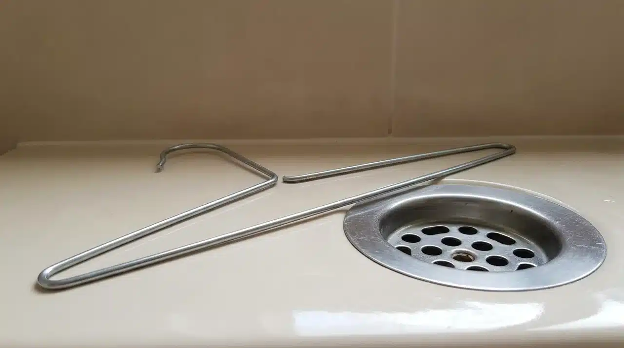 Bent wire hanger beside a sink drain, ready to remove clogs from pipes.