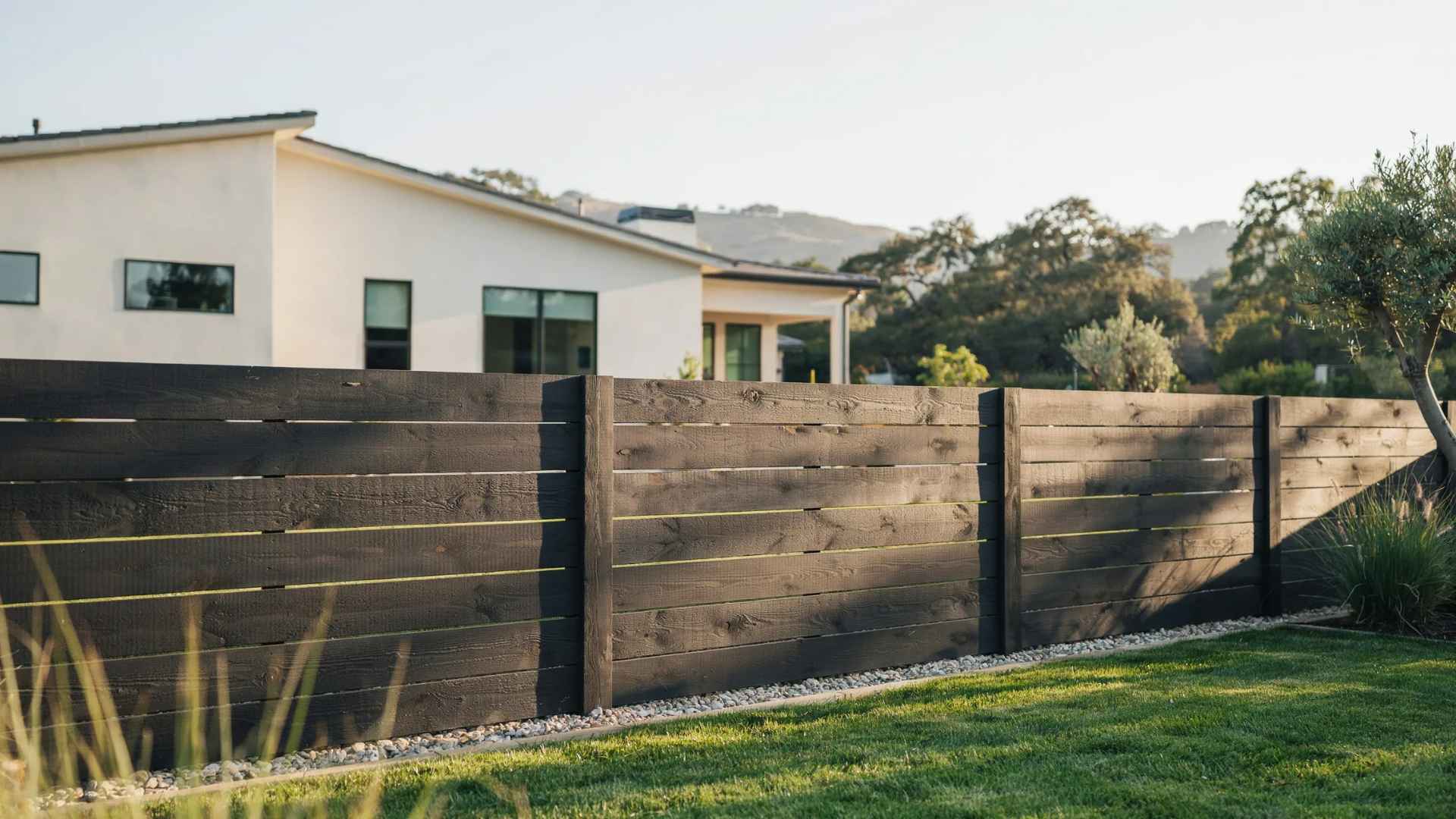 Dark-stained horizontal wood fence adding contrast beside a modern light-colored home.