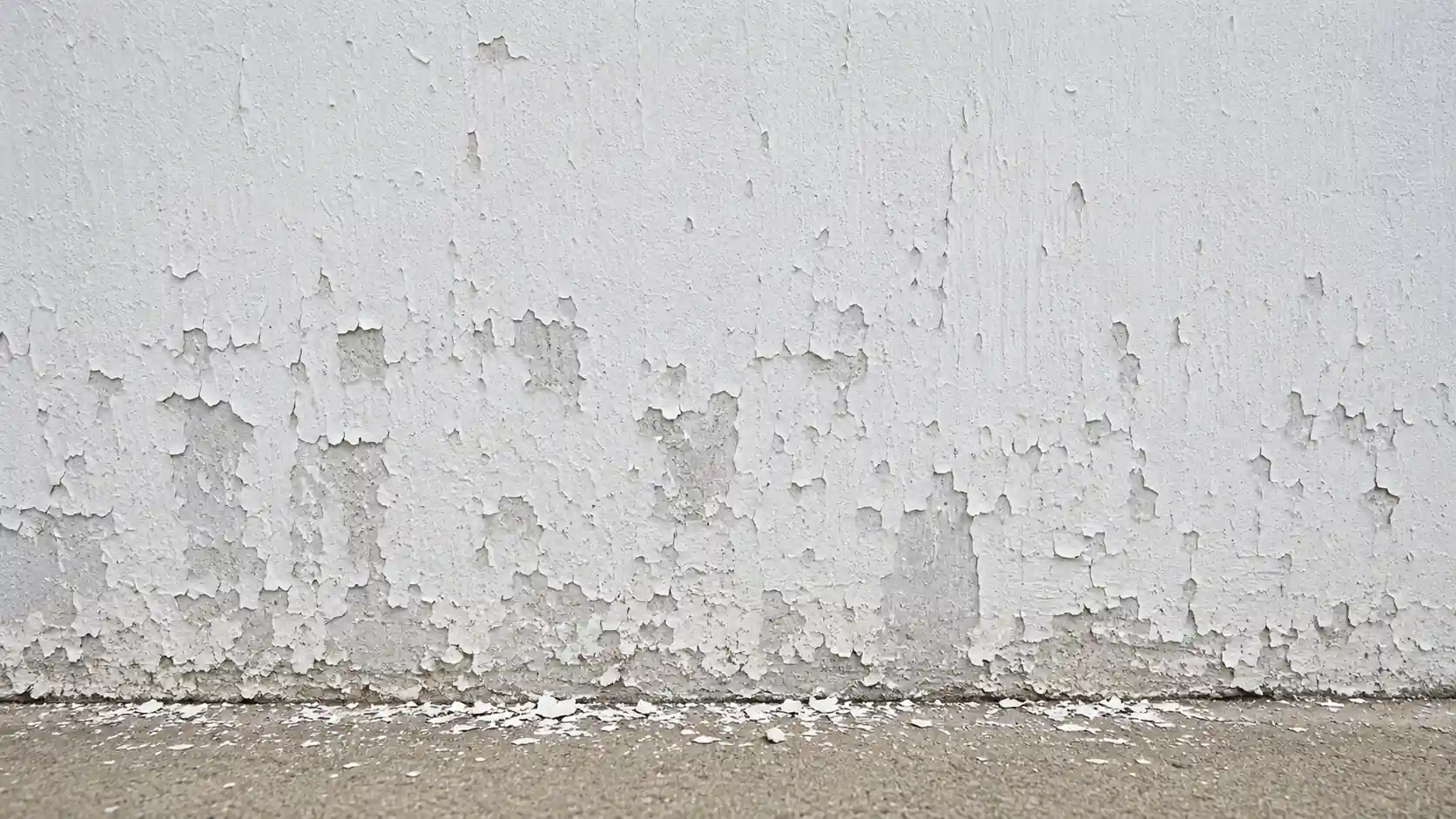 Peeling white paint on wall with large flaking sections, and scattered chalk like paint dust along the ground.