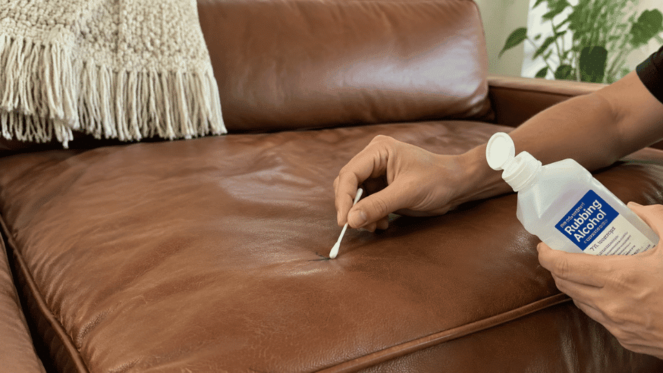 Person removing an ink stain from a leather couch using a cotton swab and rubbing alcohol.
