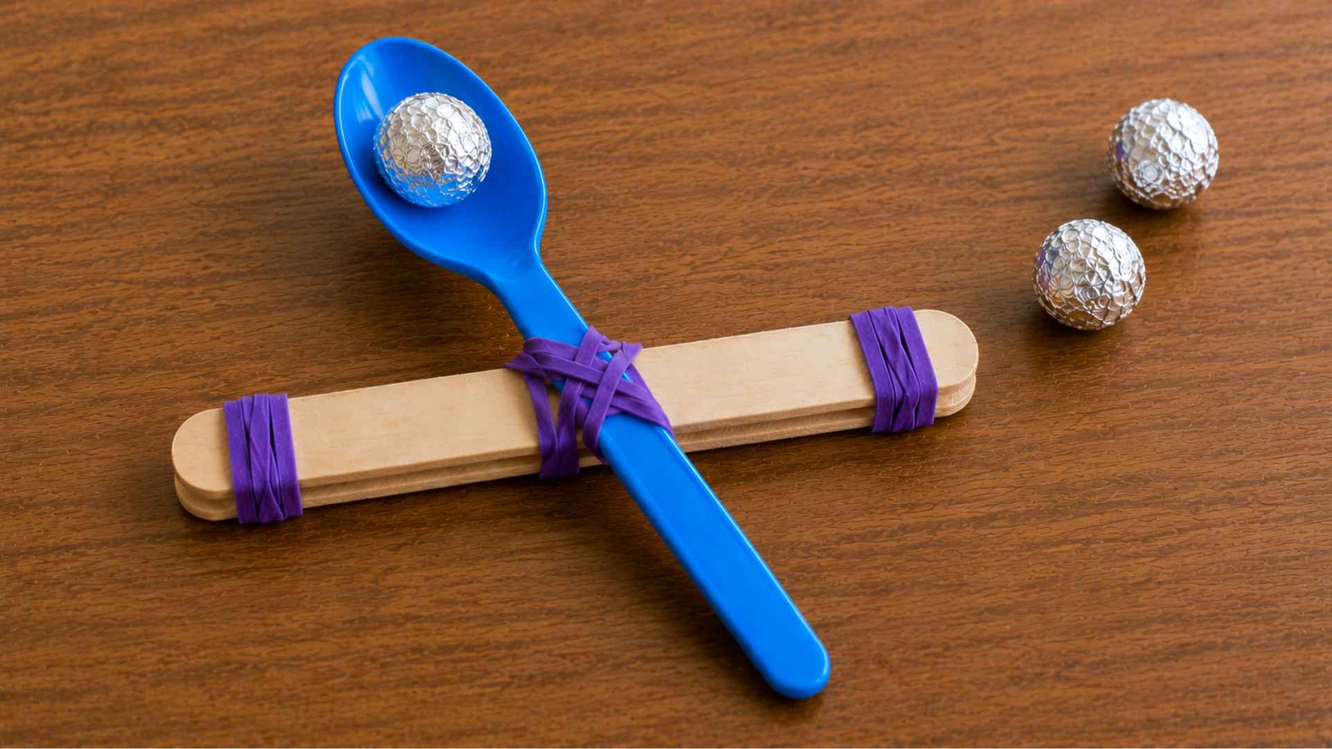 Foil ball placed inside blue spoon of finished popsicle stick catapult.