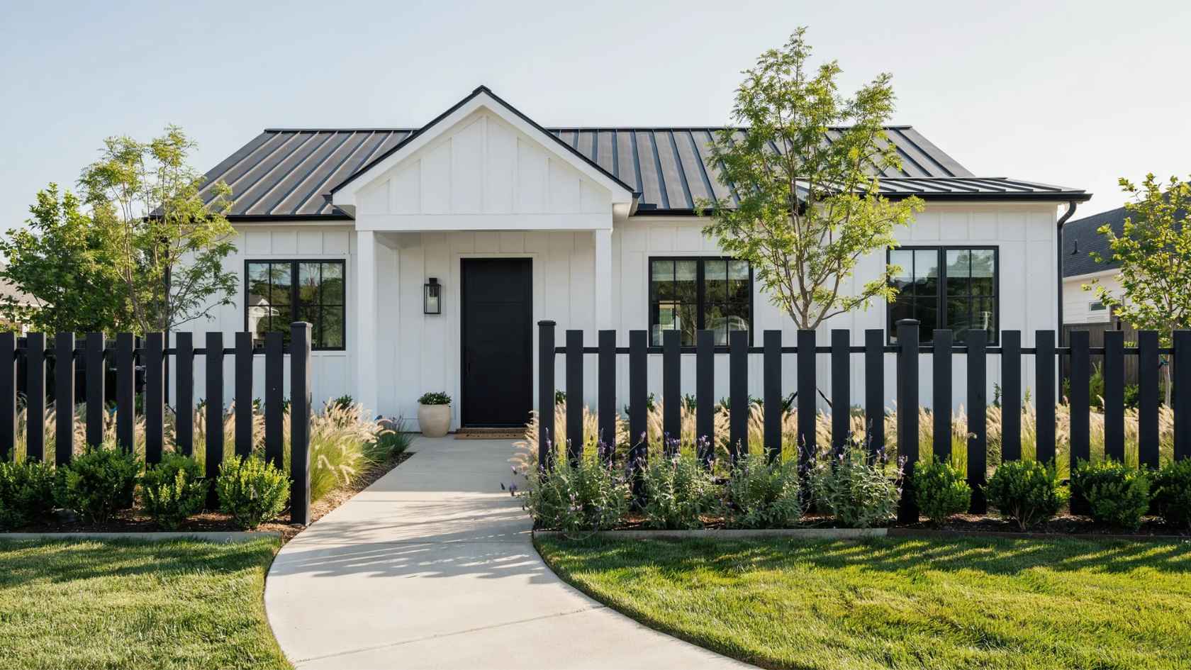 Modern black picket fence with wide boards framing a stylish front yard and contemporary home.