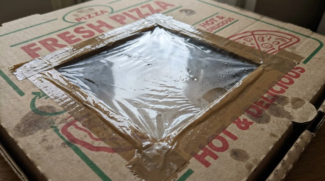 Clear plastic wrap taped tightly over the opening in a pizza box to trap heat inside the solar oven