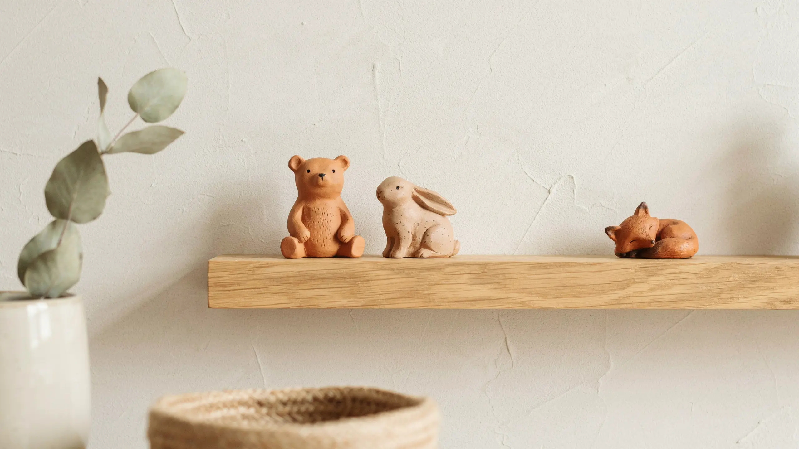 Handmade clay animal figurines a bear, rabbit, fox, and bird isplayed on a wooden shelf against a textured wall in soft natural light.
