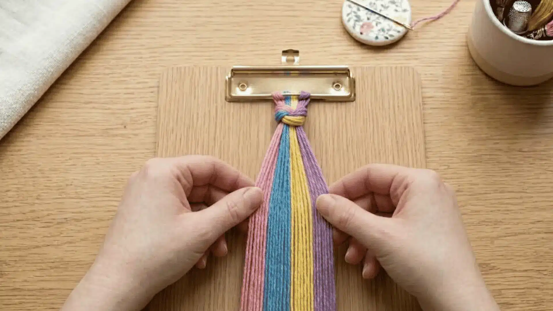 Hands arranging secured embroidery floss strands into a color pattern before making a friendship bracelet.