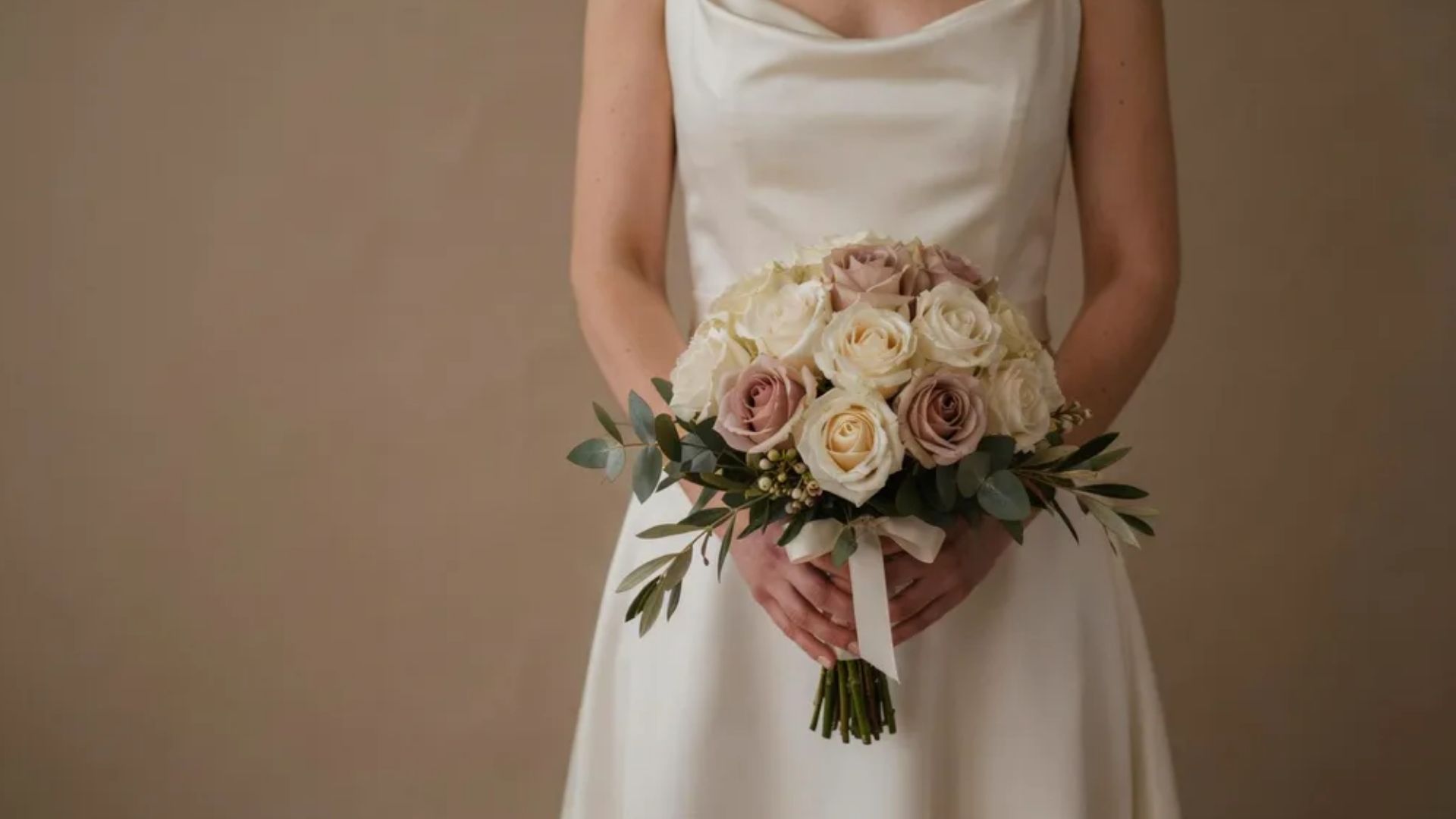 Artificial wedding bouquet with realistic silk roses and greenery held by bride in studio soft neutral backdrop