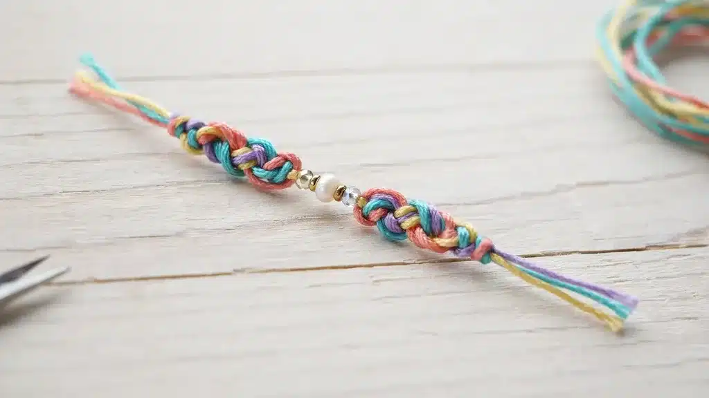Pastel braided friendship bracelet with pearl and crystal beads on a white wooden surface.