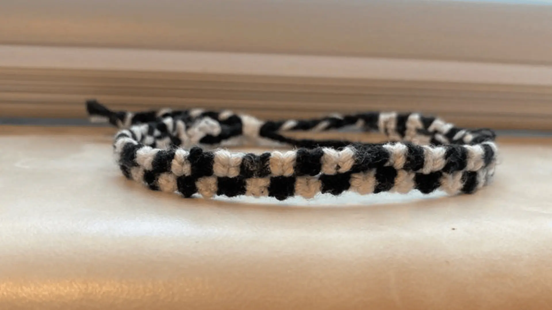 A woven friendship bracelet with a black and white checkerboard pattern resting on a light-colored surface.