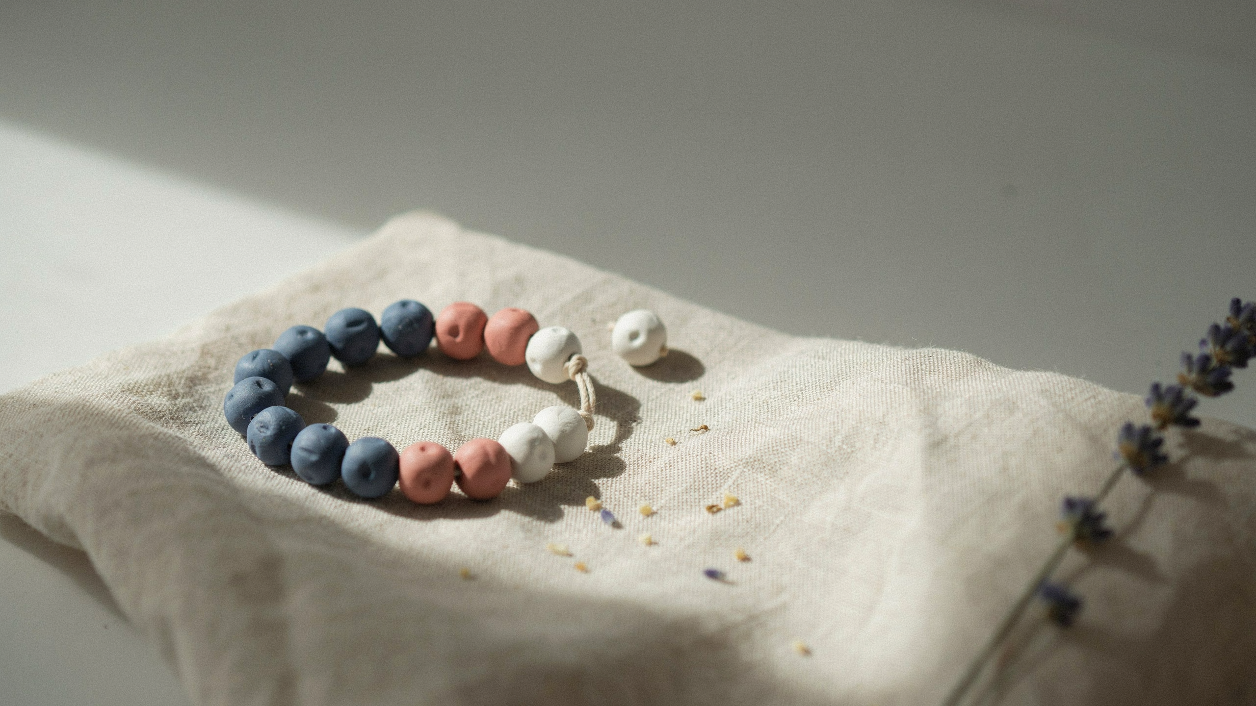 A handmade clay bead bracelet featuring evenly spaced pastel colored round beads threaded on elastic cord, displayed on neutral background with soft natural lighting.