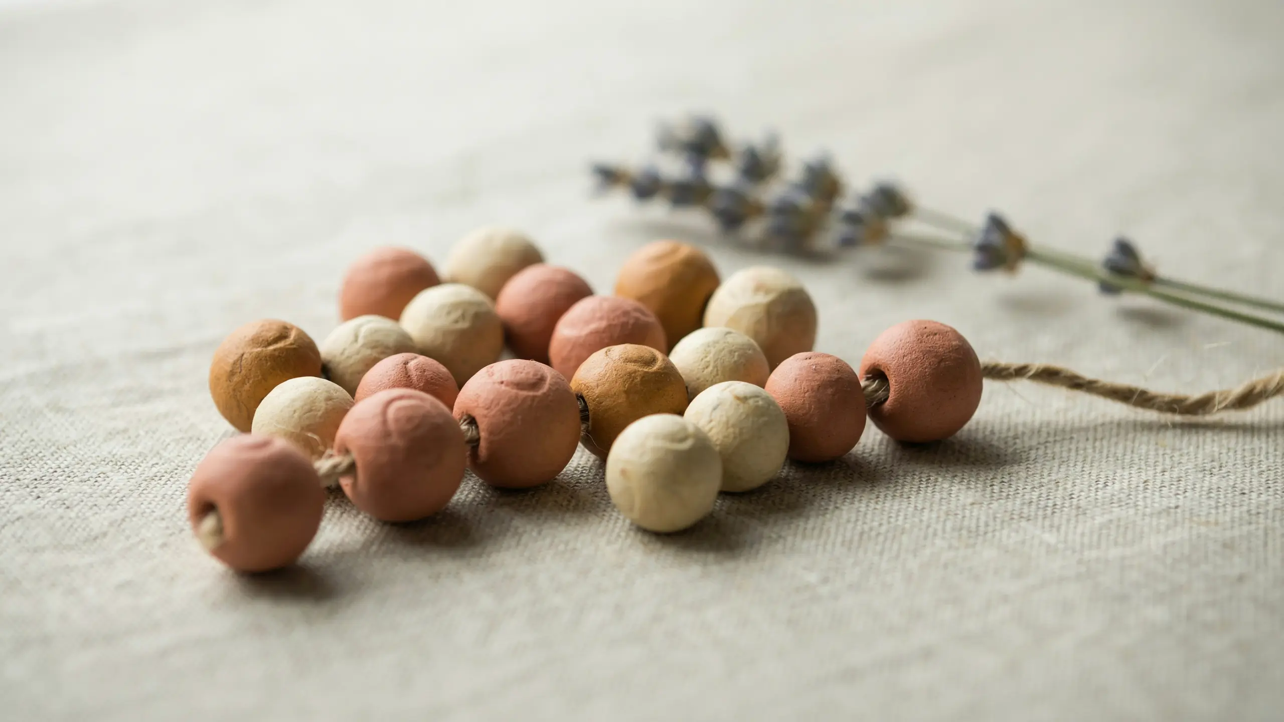 Scattered handmade clay beads in earthy tones drying on fabric with soft natural light.