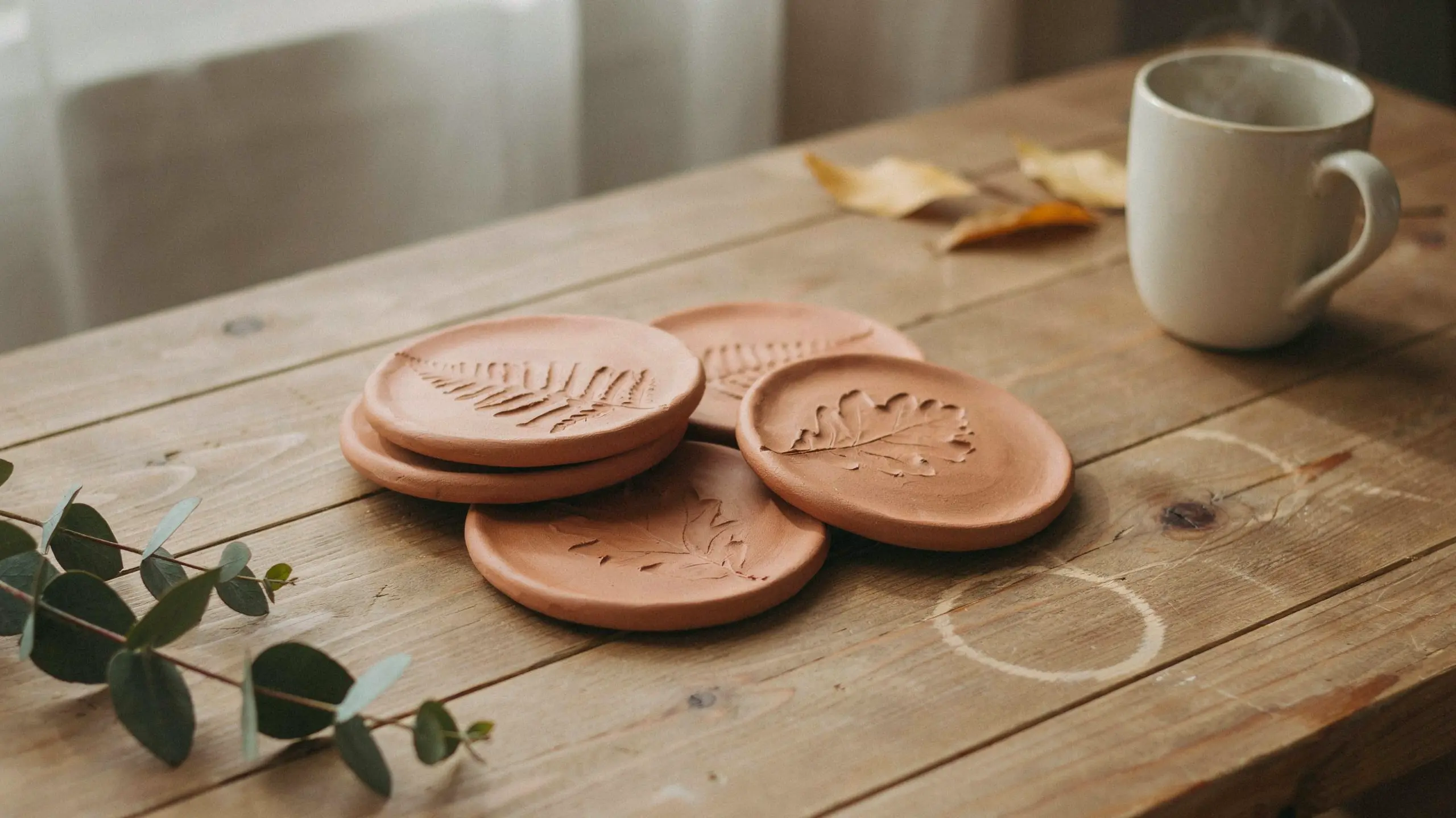 Round clay coasters with pressed leaf textures stacked on a rustic wooden table.