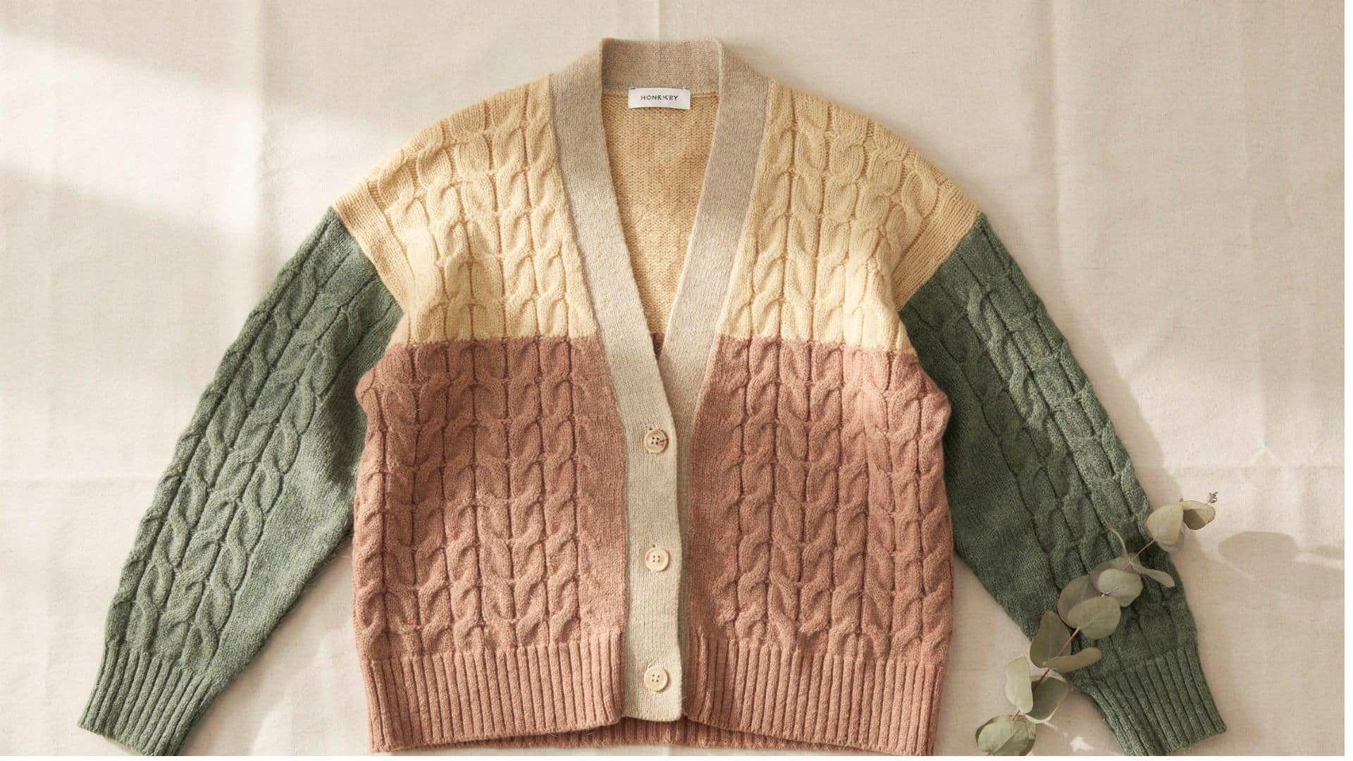 Color-block cable knit cardigan featuring cream, dusty pink, and sage green panels with button-front closure and ribbed trim.