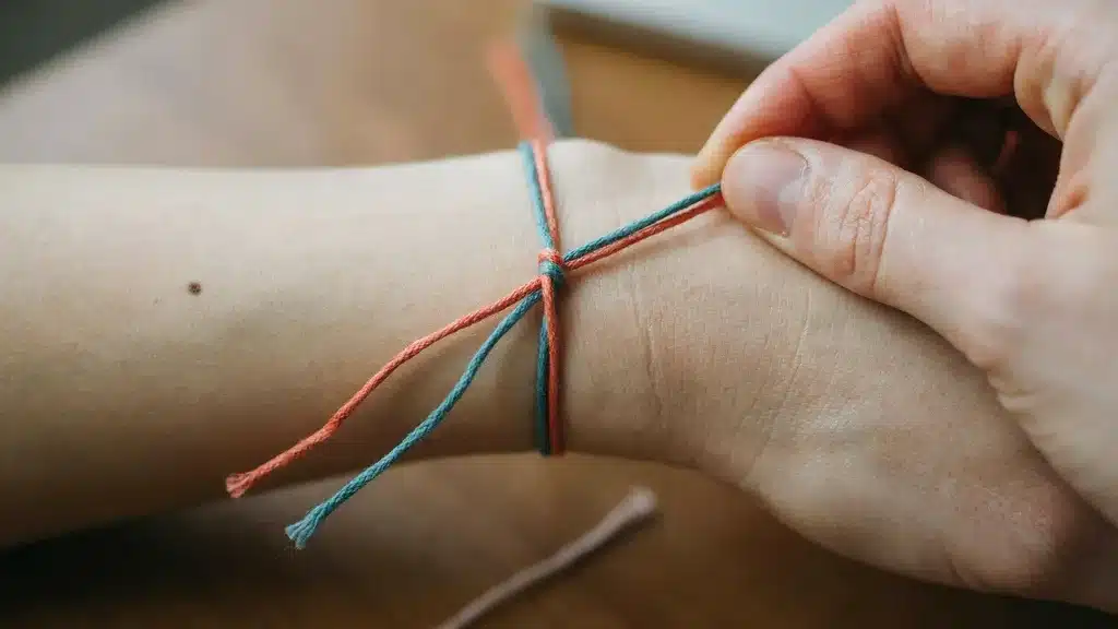 Close-up of friendship bracelet strings crossed over each other to begin tying a knot.