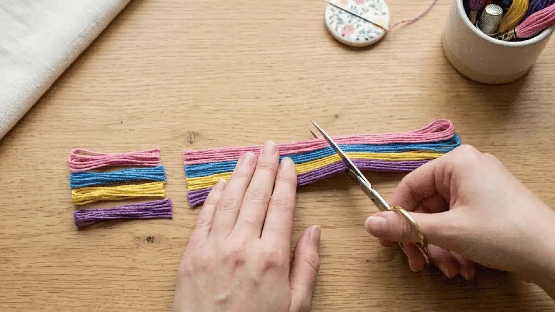 Hands cutting colorful embroidery floss strands into equal lengths on a wooden table before bracelet making.