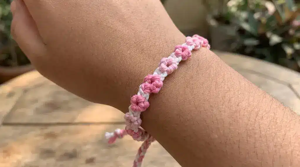 A pink and white woven flower string bracelet worn on a wrist