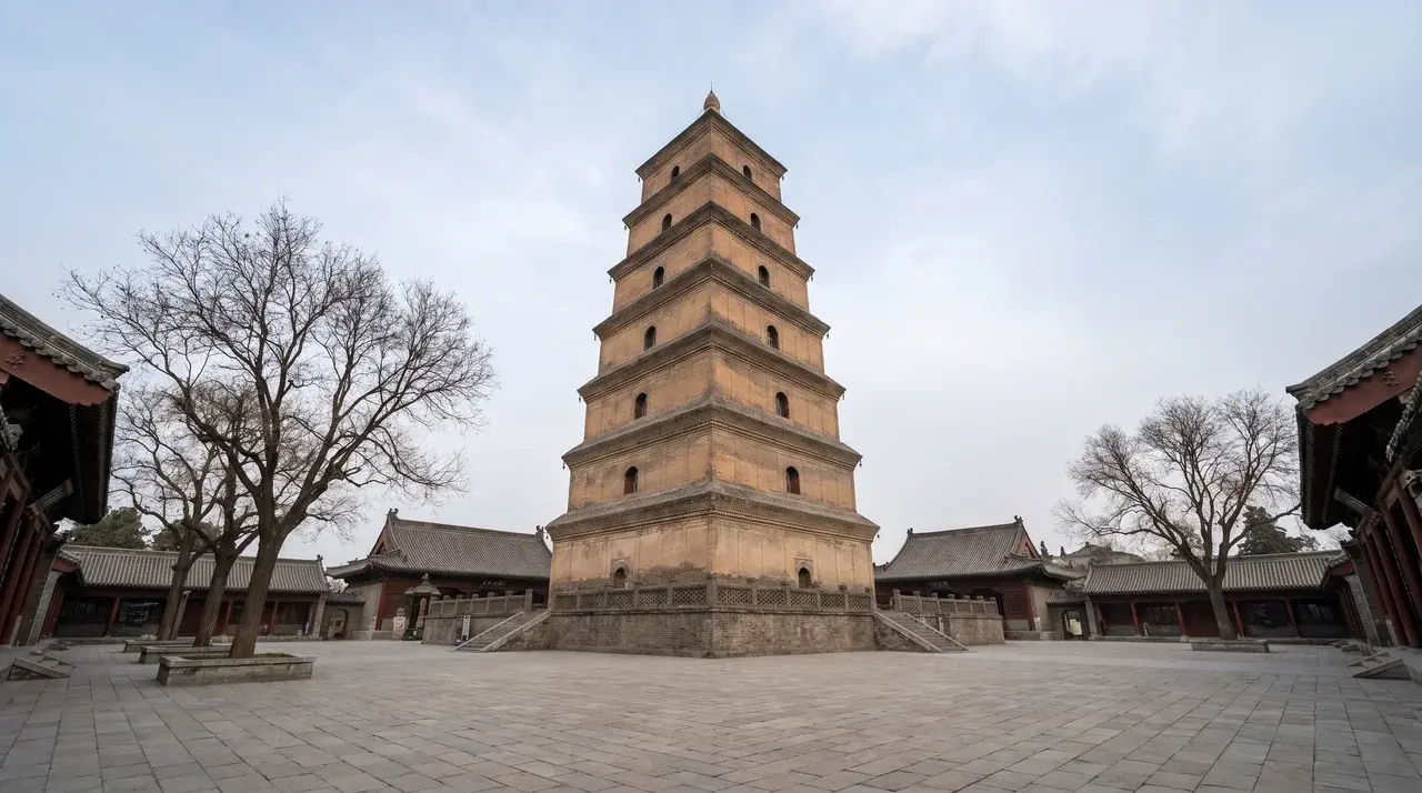 The Giant Wild Goose Pagoda in Xi'an, China, standing tall in a courtyard with surrounding traditional buildings and leafless trees under a cloudy sky.