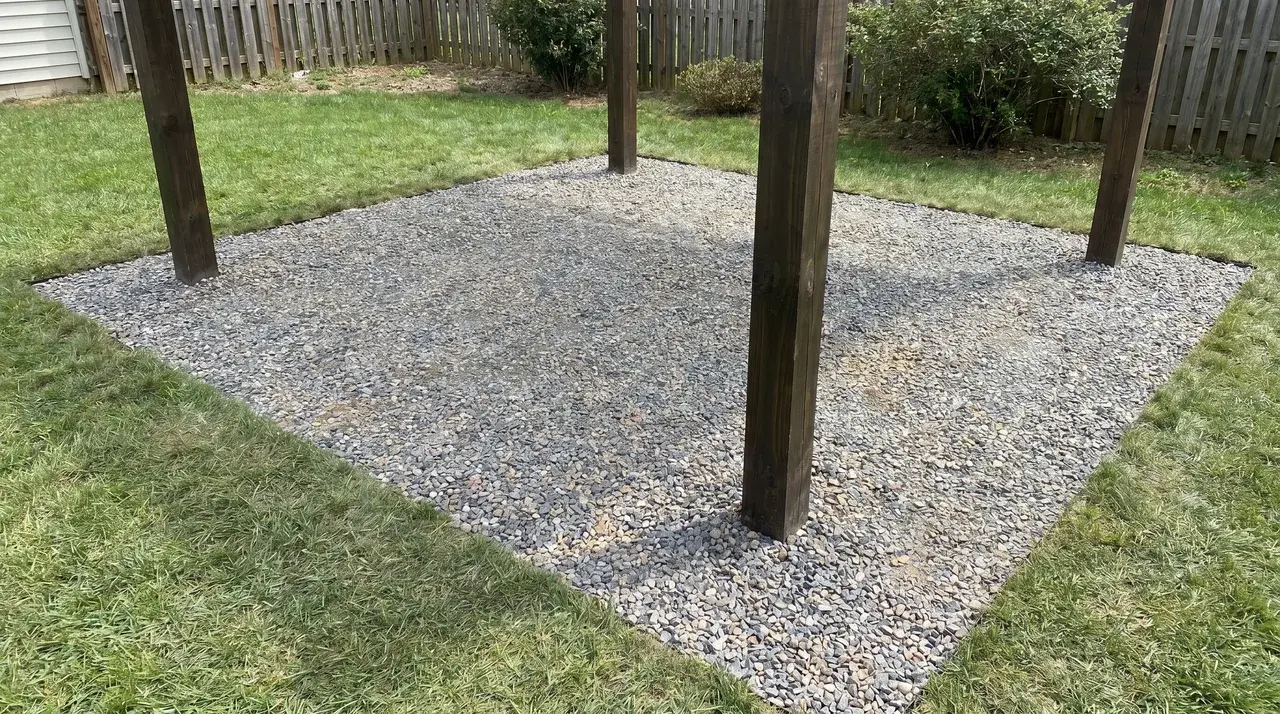 Crushed gravel surface filling a pergola footprint and extending beyond the posts on each side