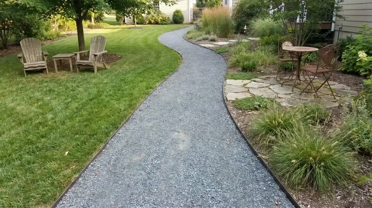 Crushed gravel pathway with steel strip edging on both sides running through a residential backyard with furniture