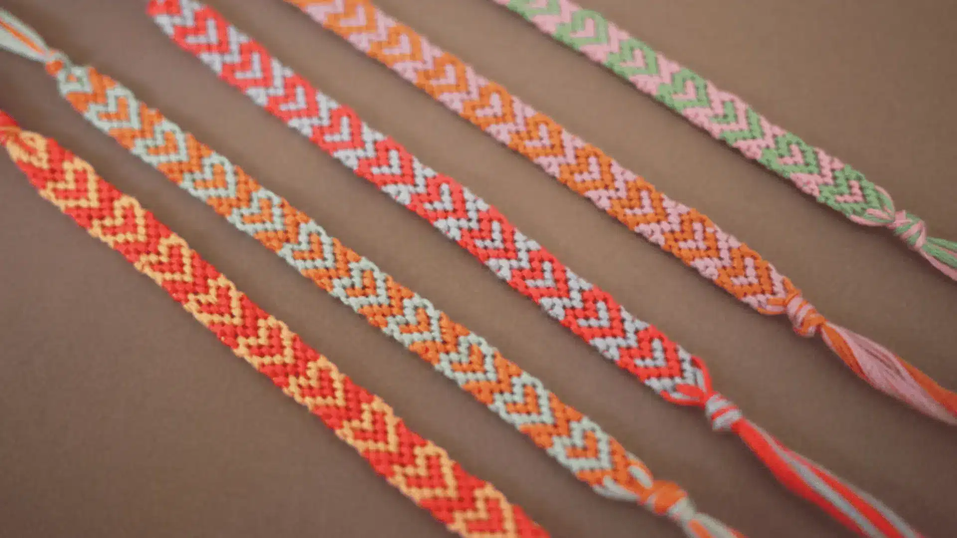 Five colorful woven friendship bracelets with heart patterns.