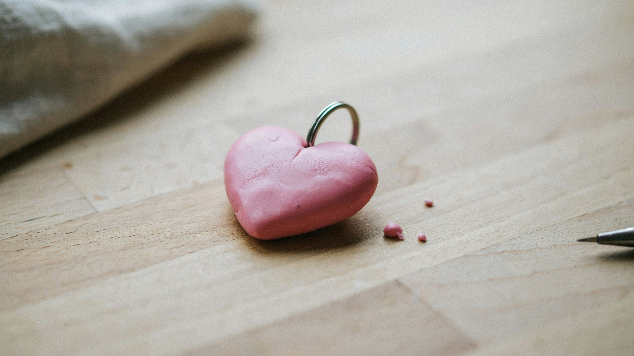 A handmade heart shaped polymer clay keychain with smooth joined teardrop forms, soft pink finish, and a small hole for attachment, placed on wooden surface.