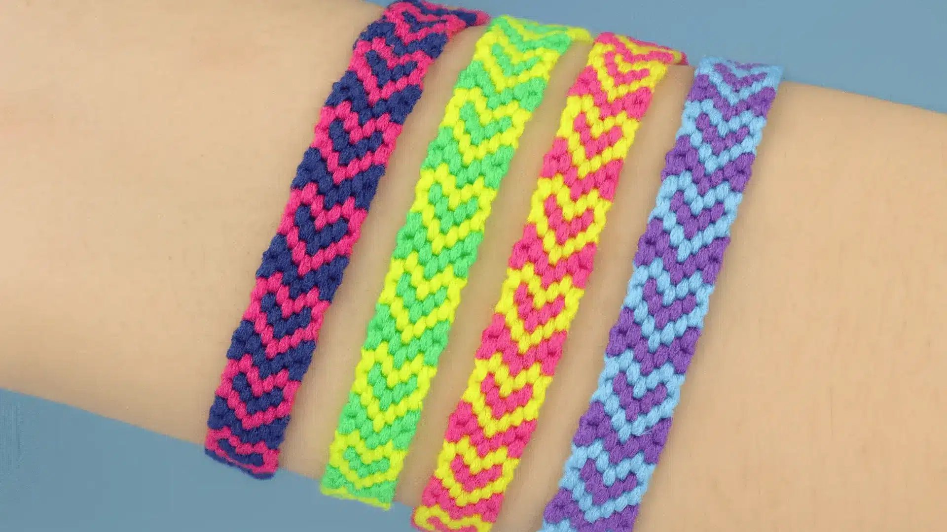 Four colorful woven friendship bracelets with a hearts pattern lined up on a person's wrist.