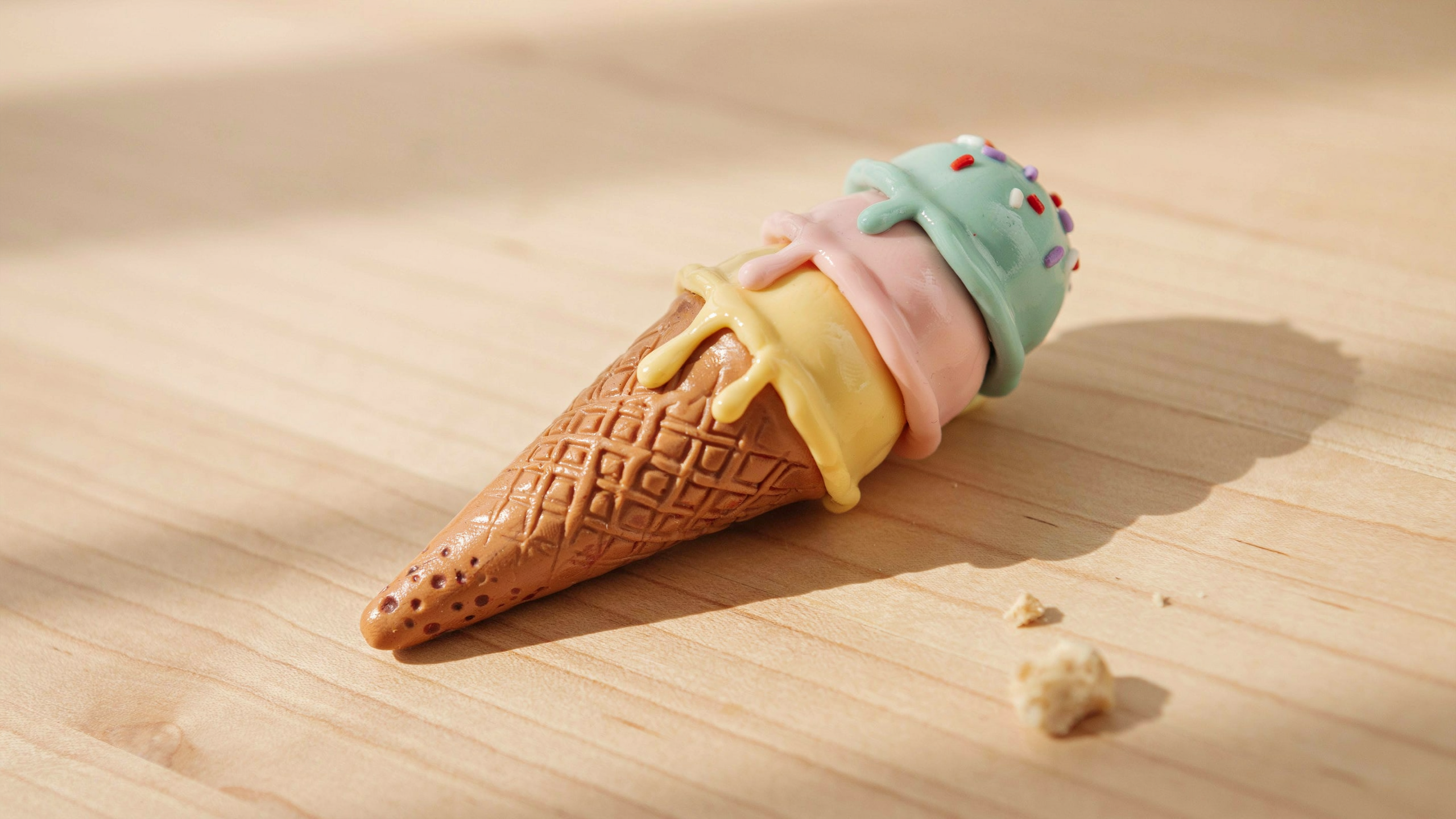 A colorful handmade polymer clay ice cream cone charm lying flat on a wooden table, featuring pastel scoops, waffle cone texture, and soft glossy drip details.