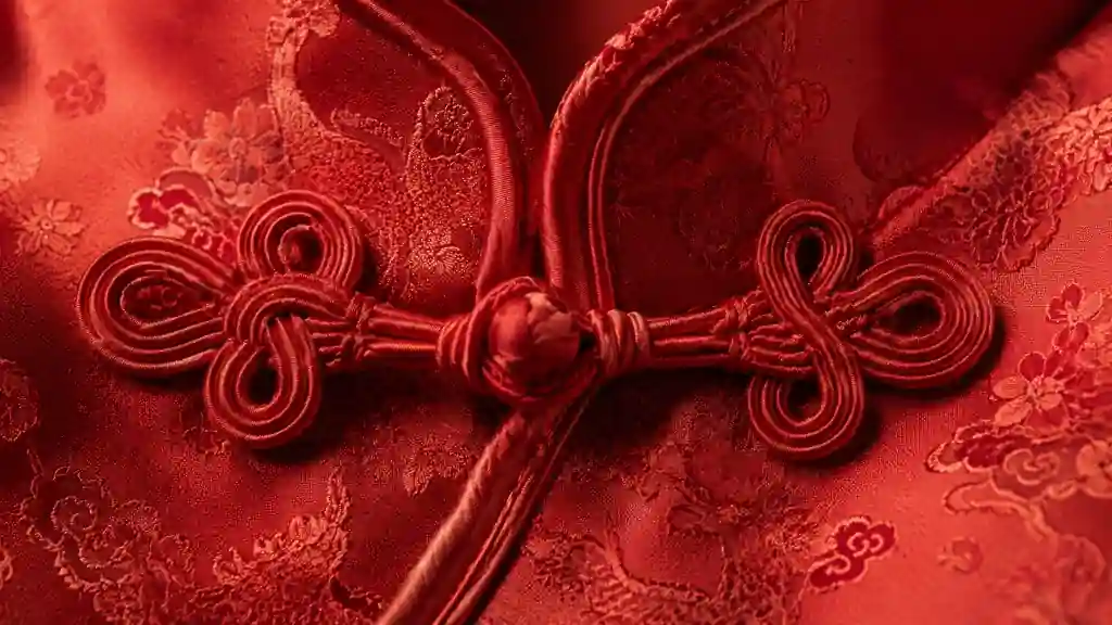 An intricate red silk Chinese frog closure button with decorative woven knots fastened on a matching embroidered silk garment.