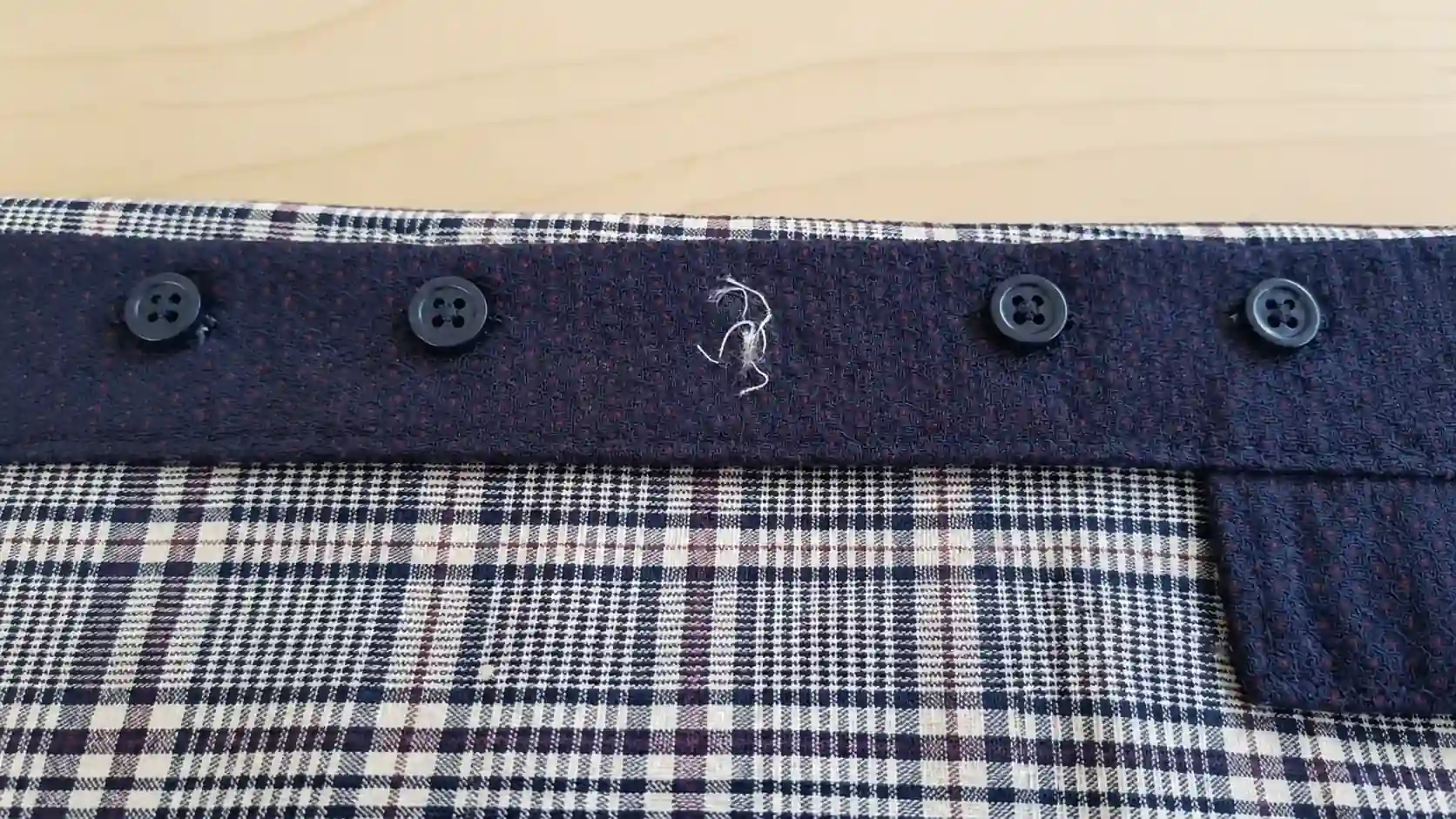 A close-up of a plaid shirt collar with a loose thread.