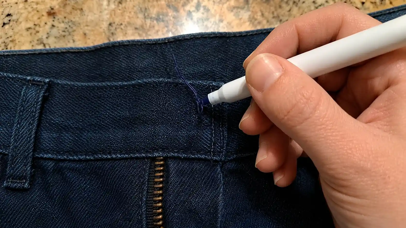 Hand marking the button placement spot on blue denim jeans.