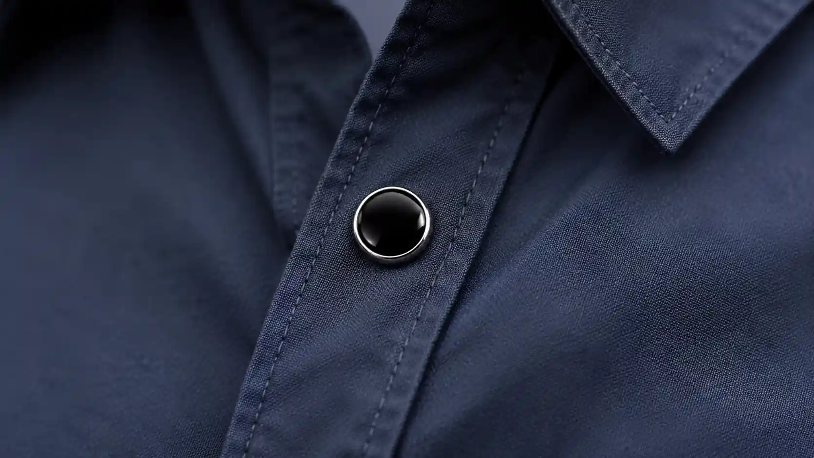Close-up of a black enamel stud button on a navy shirt placket, highlighting polished details.