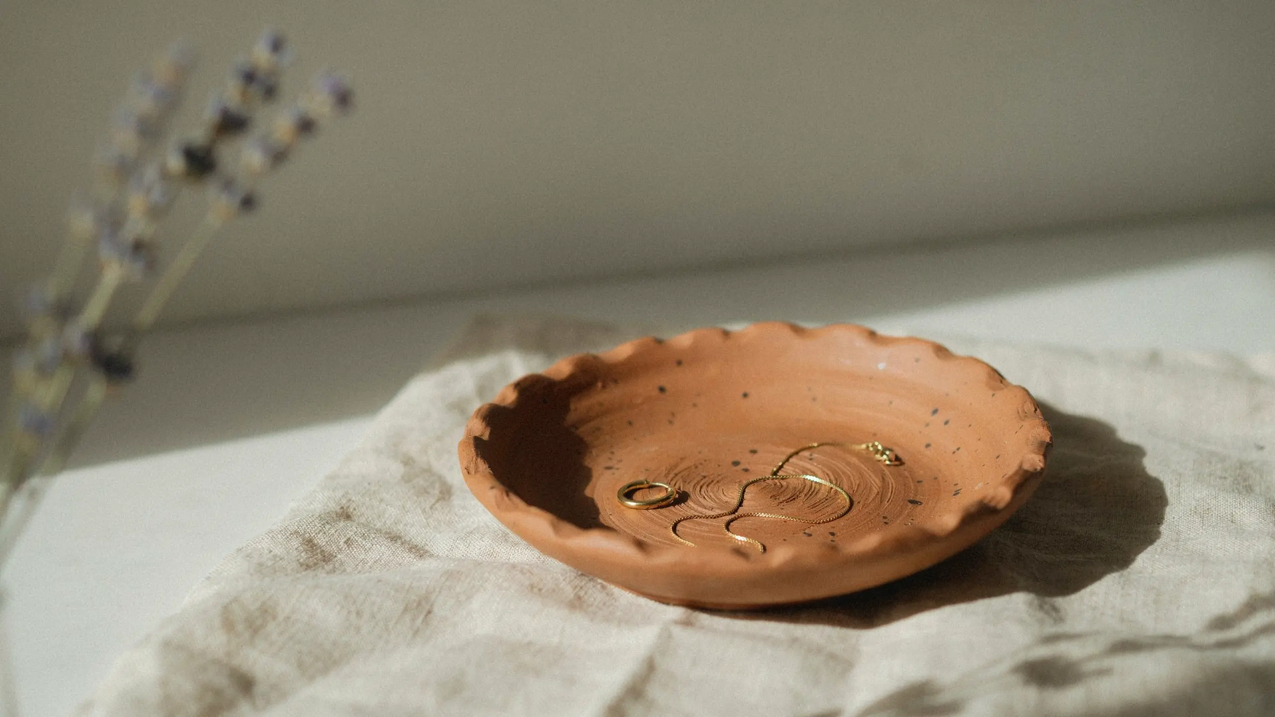 Handmade clay jewelry dish with subtle texture holding small rings in soft natural light.