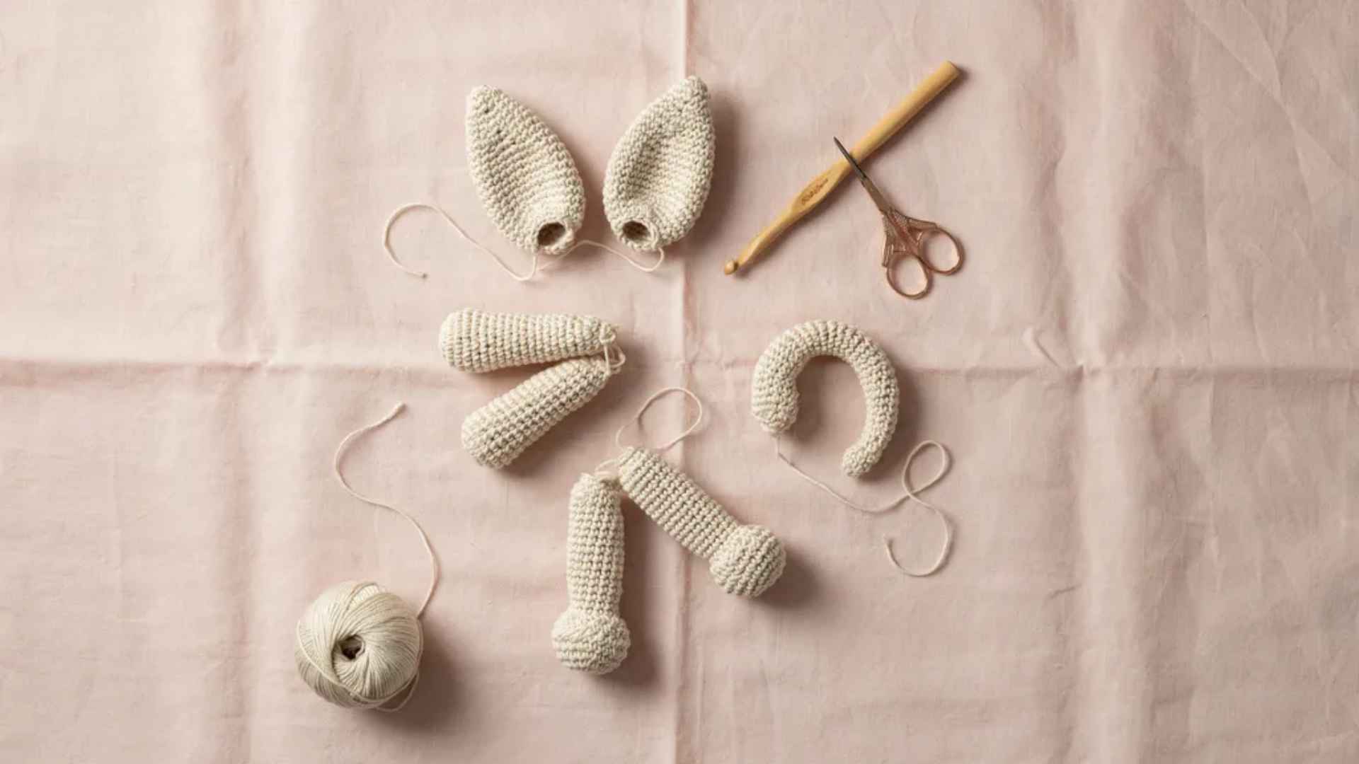 Small crochet animal parts like ears and limbs made separately with yarn tails ready for assembly on soft fabric
