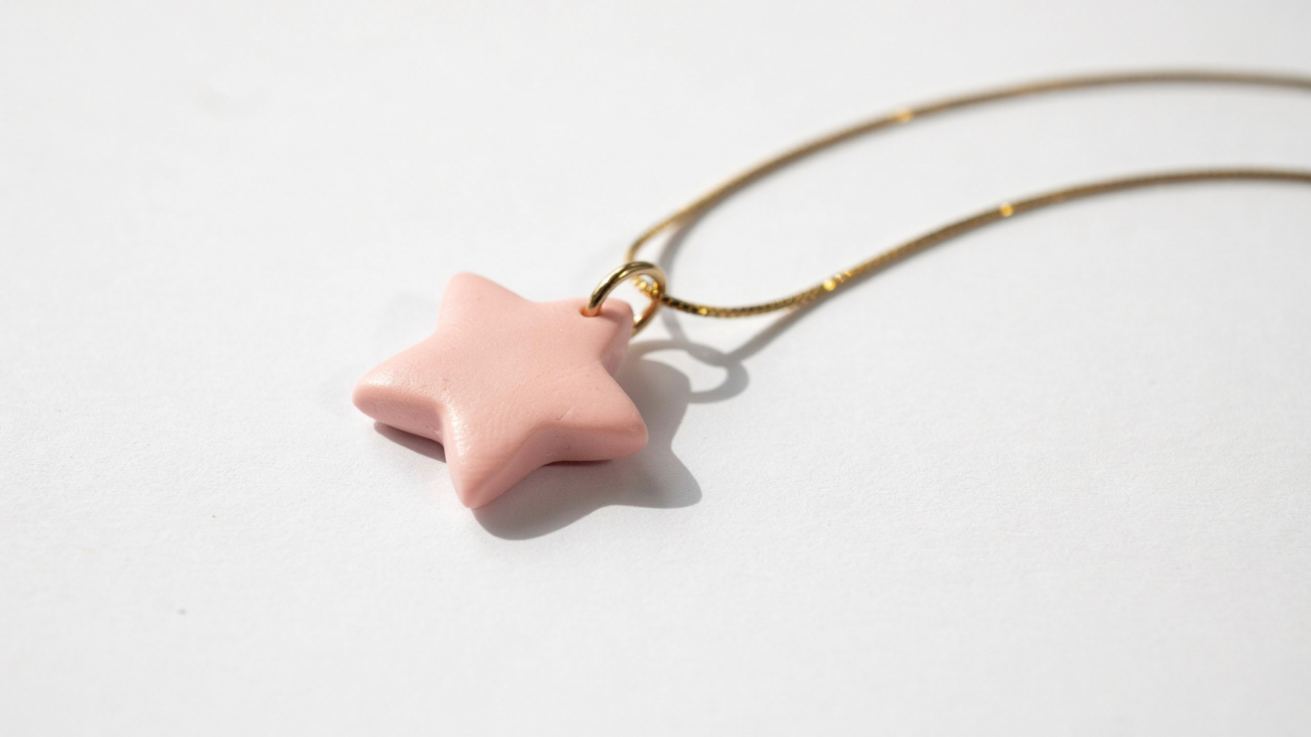 A small handmade polymer clay pendant necklace charm shaped like a star, with a jump ring and chain, shown on minimalist background with soft light.