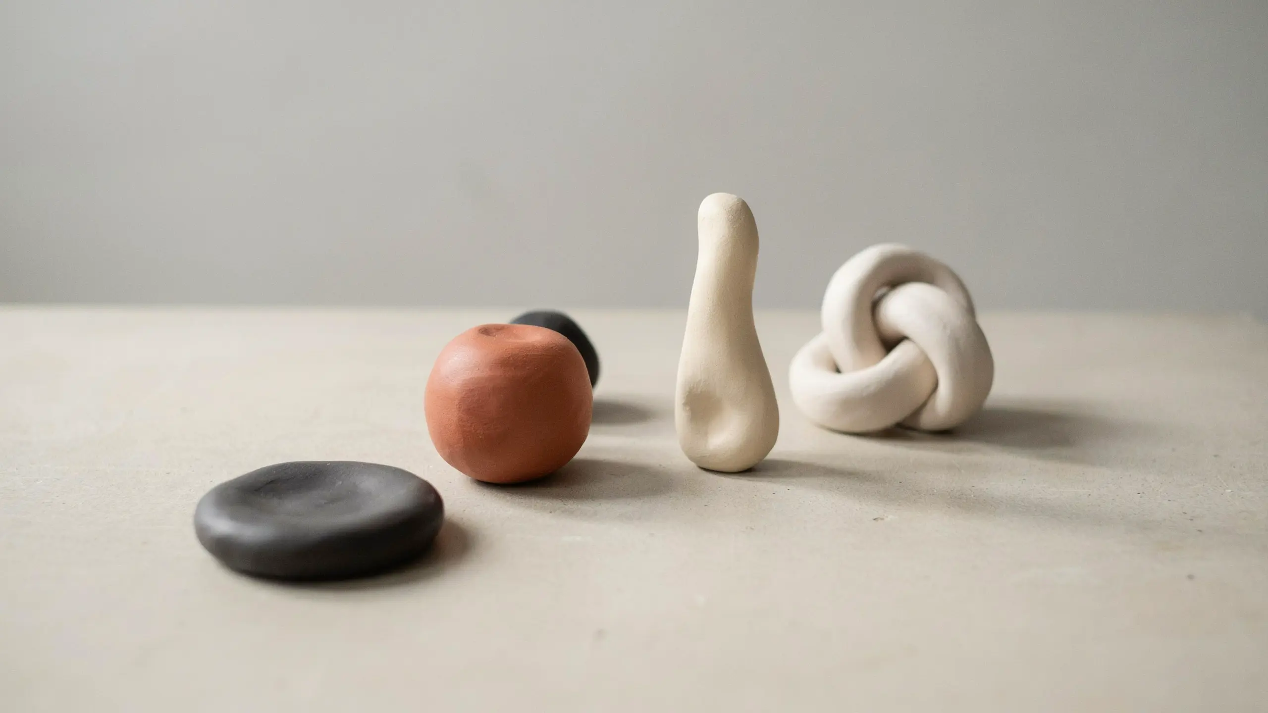 Small abstract handmade clay forms arranged on a table with minimal styling and soft shadows.