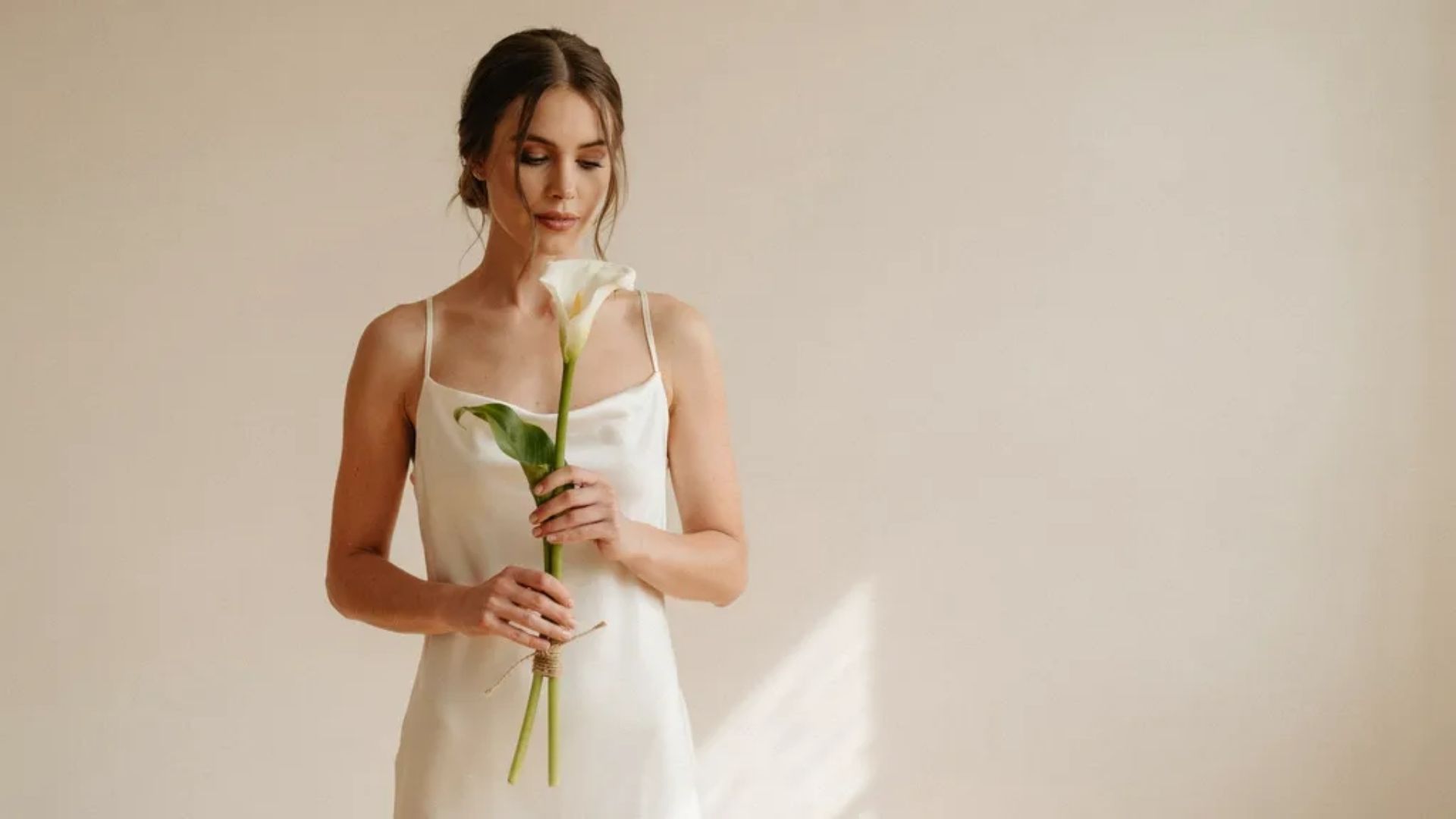 A minimal bridal bouquet featuring a single white rose held by bride in clean neutral background with soft natural light