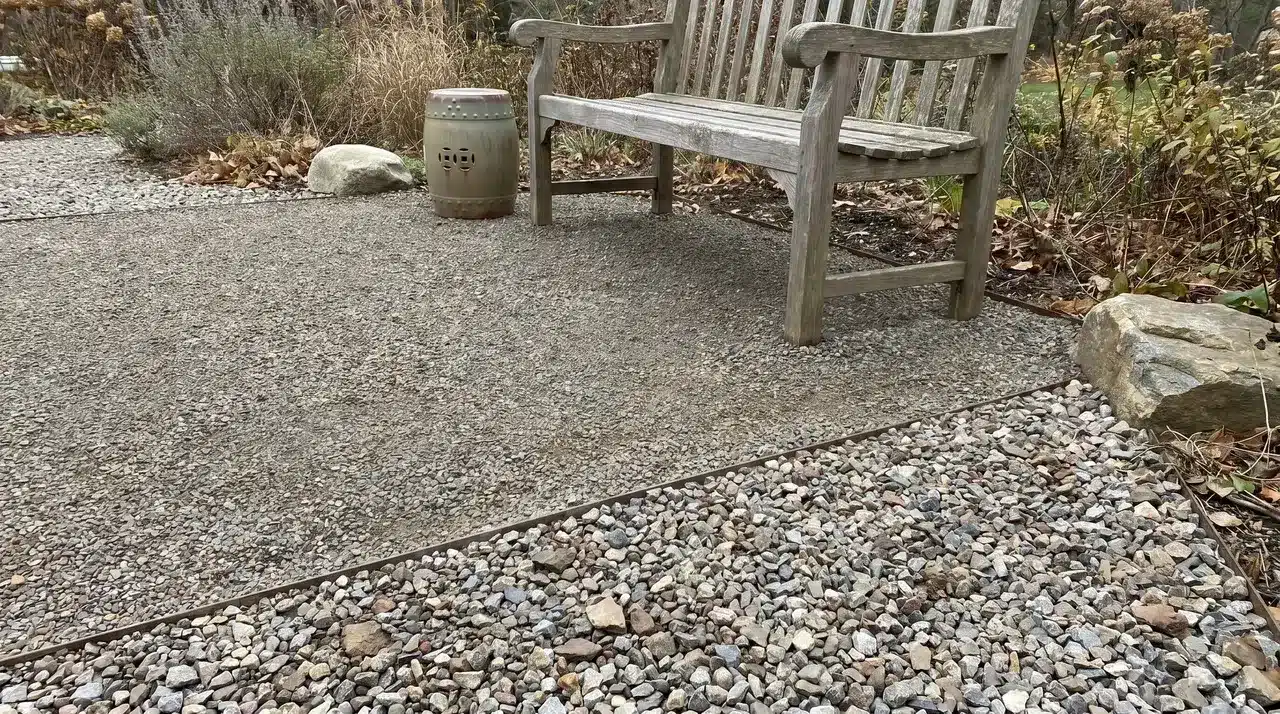Cross-section of gravel surface showing coarser base layer beneath finer finish gravel at a cut edge