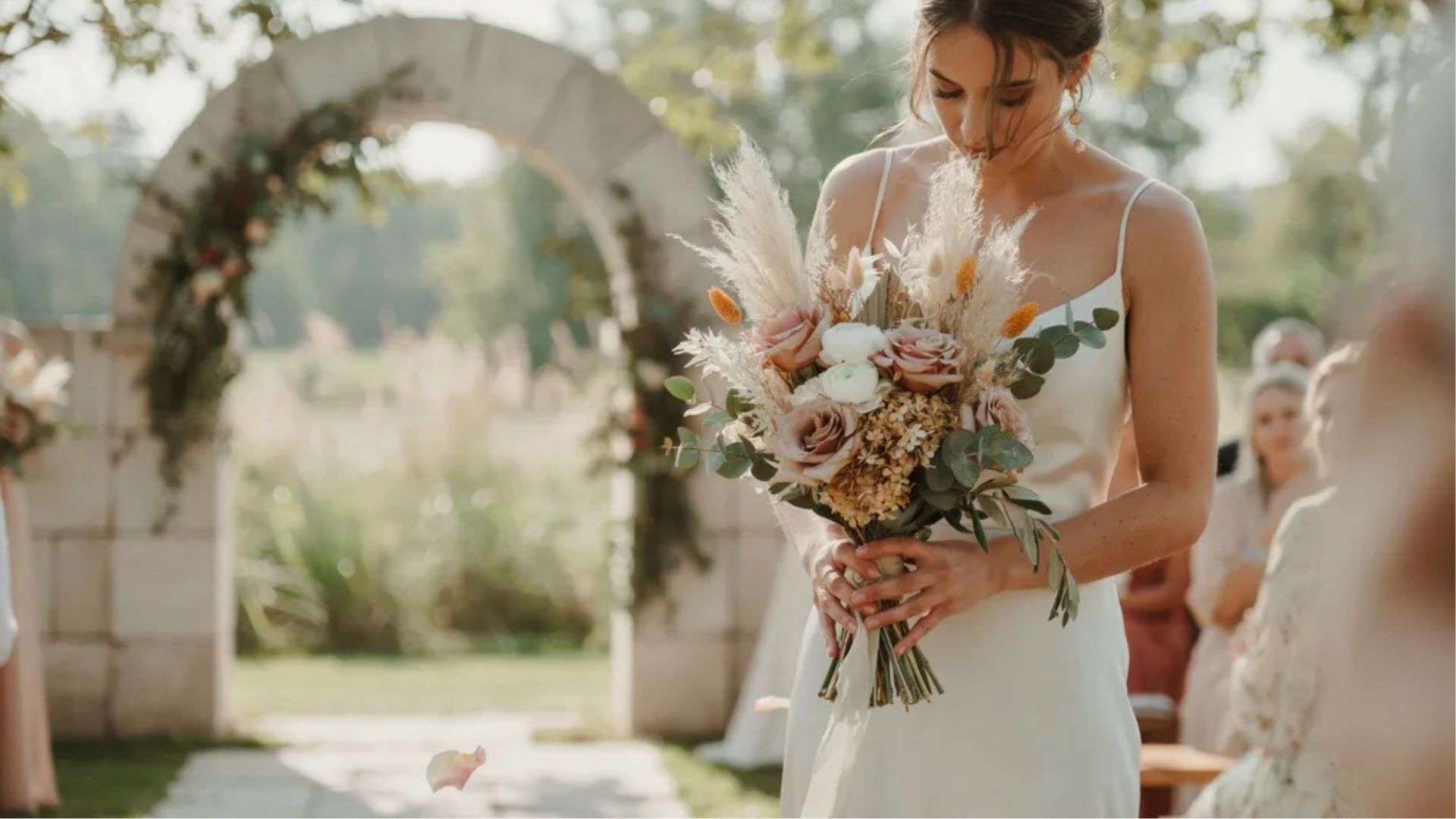 Mixed texture wedding bouquet combining fresh blooms dried stems and greenery held by bride in outdoor ceremony