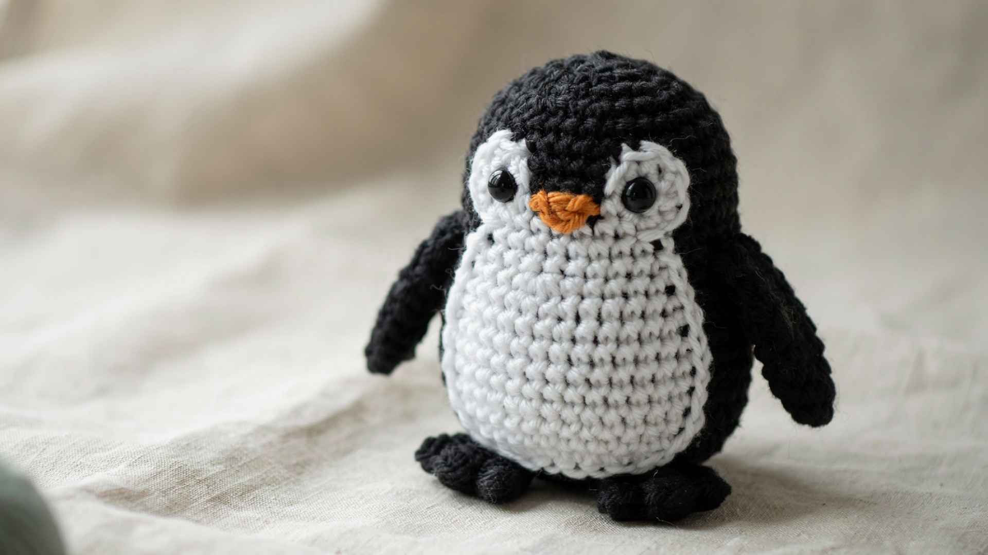 Crochet penguin amigurumi black white body small wings beginner project assembled on soft neutral fabric background