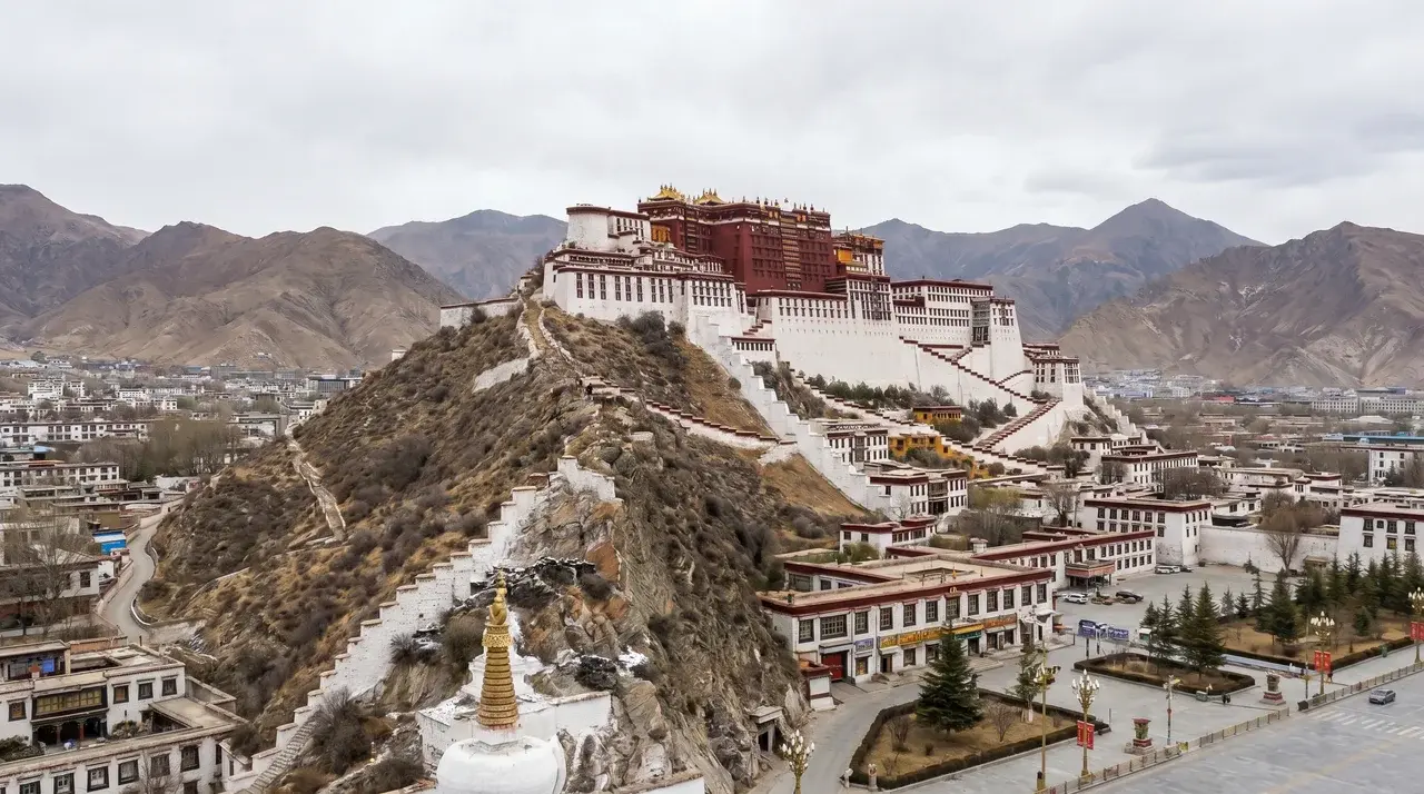 Potala Palace in Lhasa, Tibet, perched on a hill with white and red walls, terraces, and golden roofs, overlooking the surrounding city and mountains.