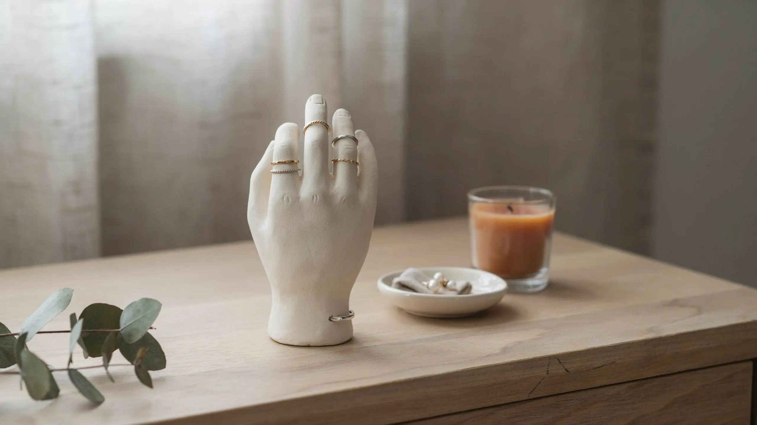 Clay hand-shaped ring holder with rings placed on fingers in soft indoor lighting.