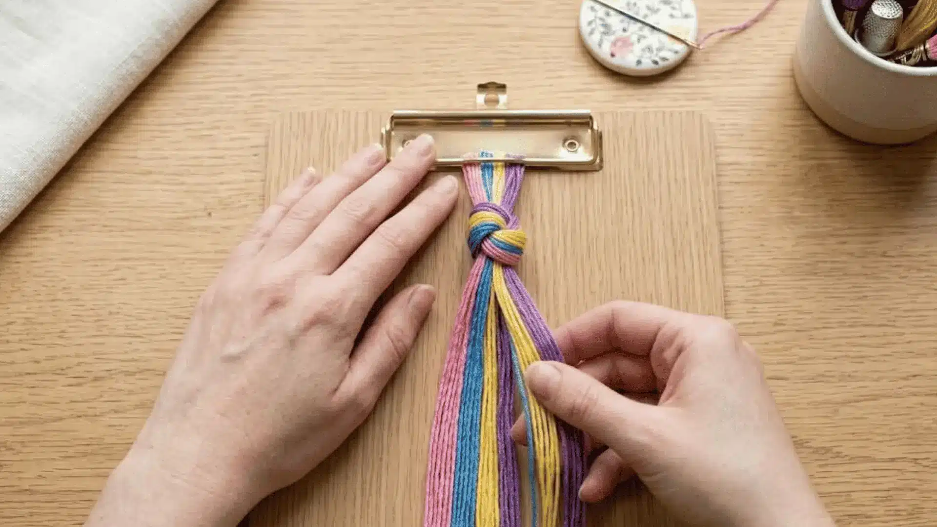 Embroidery floss strands clipped to a clipboard with hands arranging the threads for bracelet making.