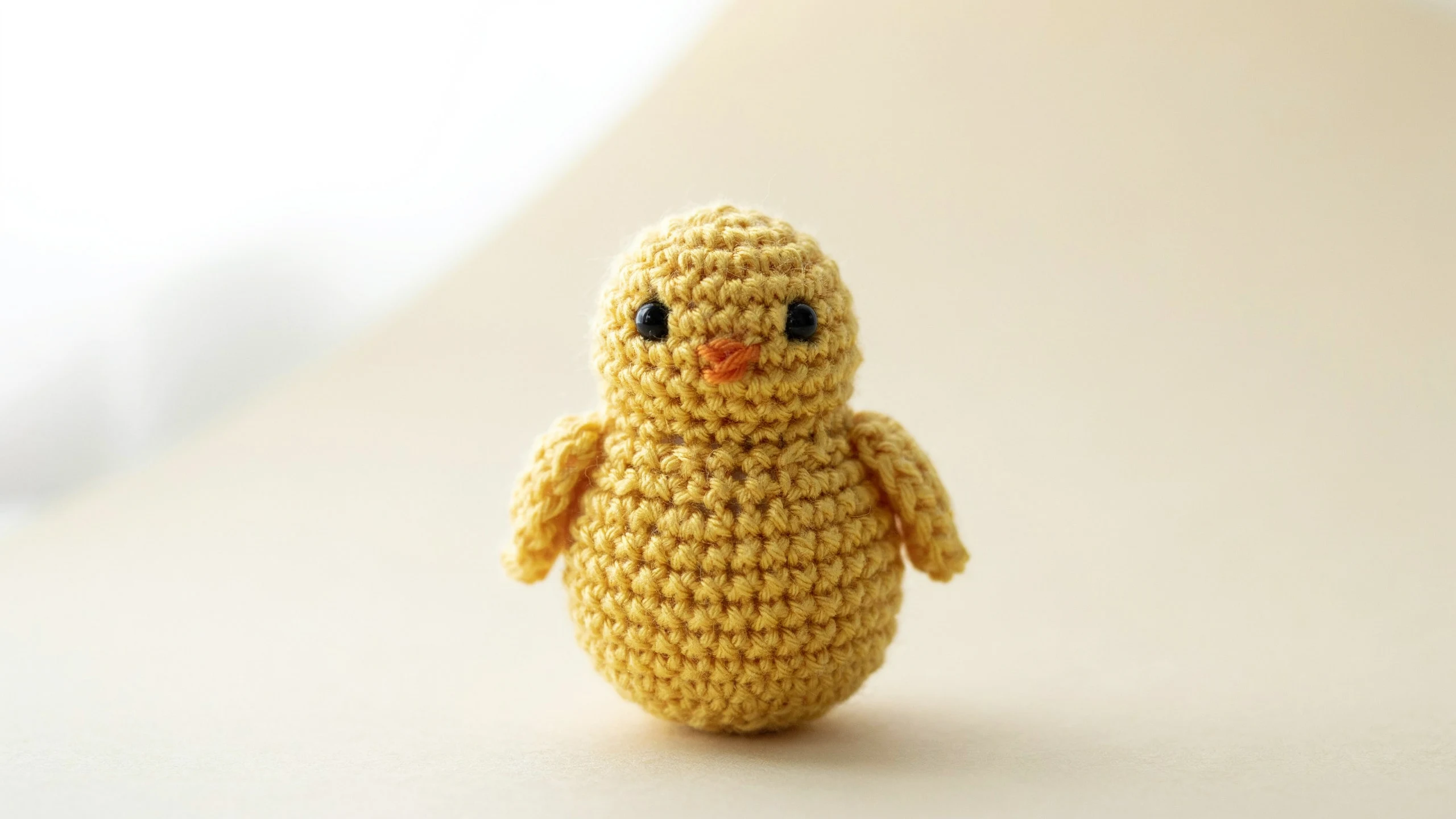 Small yellow crochet chick with flat wings and orange beak centered