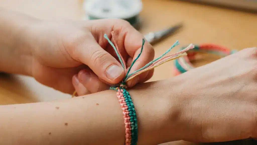 Hands tightening the first knot of a friendship bracelet around a wrist.