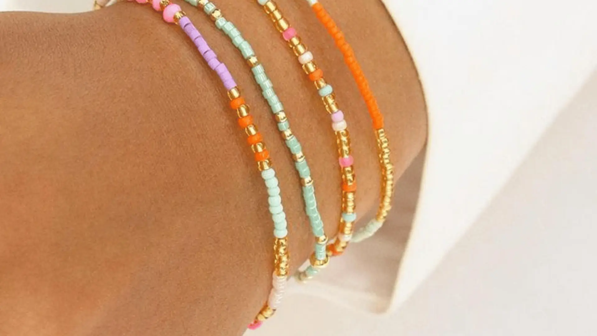 Four delicate, thin beaded bracelets with gold and colorful tiny dot bead patterns stacked on a wrist.