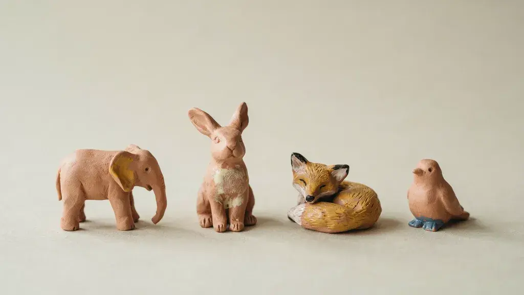 Handmade miniature clay animals including elephant, rabbit, fox, and bird with soft natural lighting on neutral background.