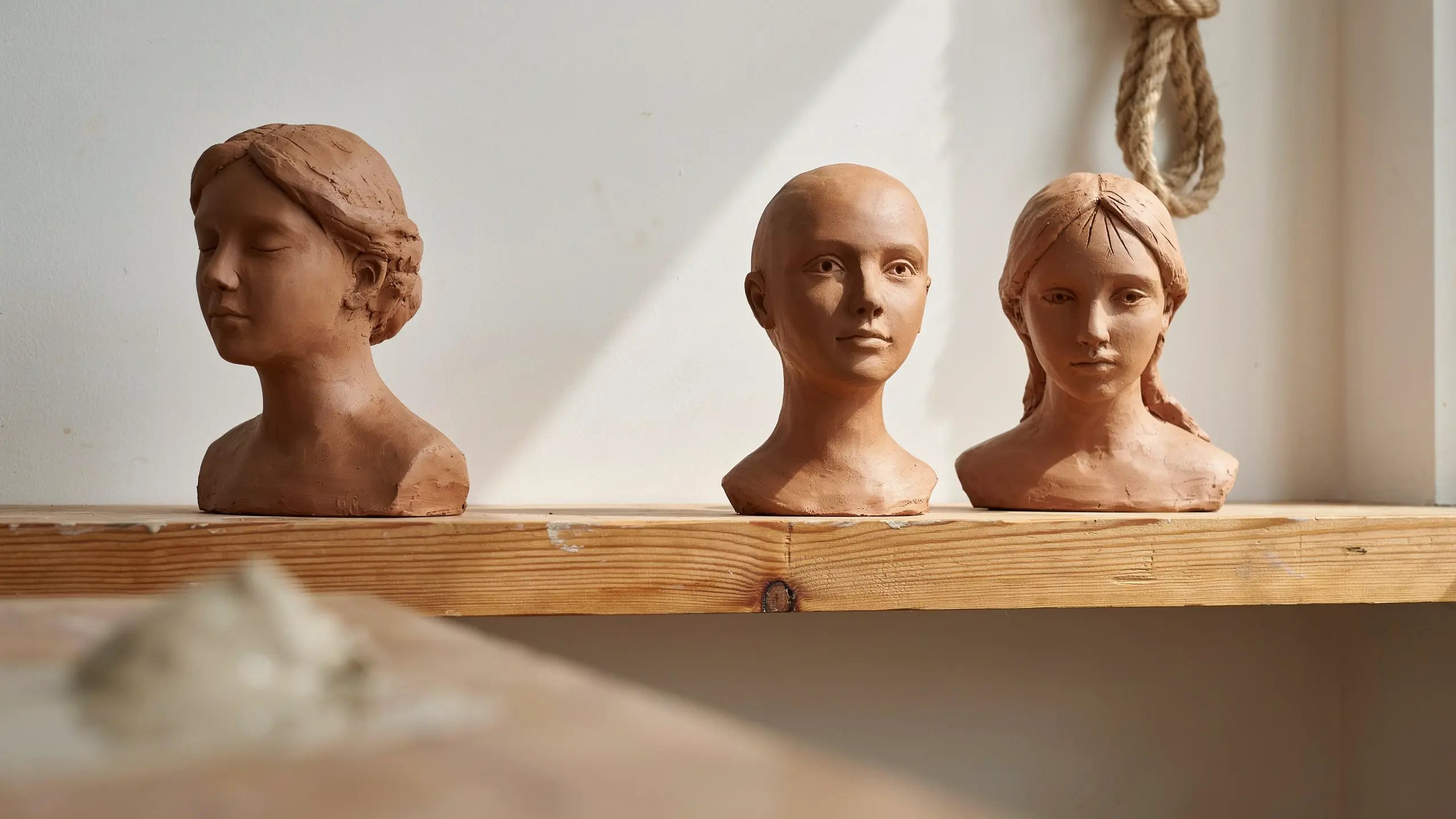 Three handmade clay bust sculptures on a wooden shelf with warm sunlight and subtle handcrafted texture details.
