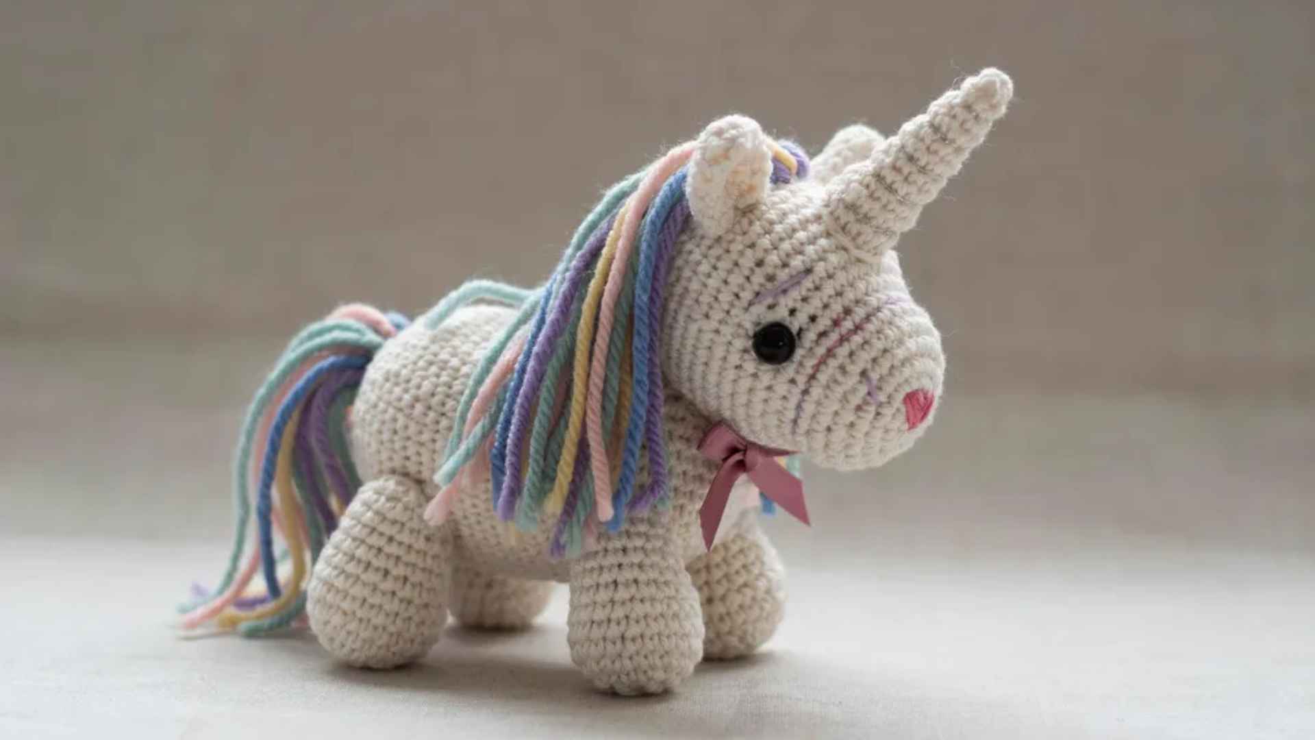 Crochet unicorn amigurumi with horn and colorful yarn mane showing detailed intermediate construction on soft background