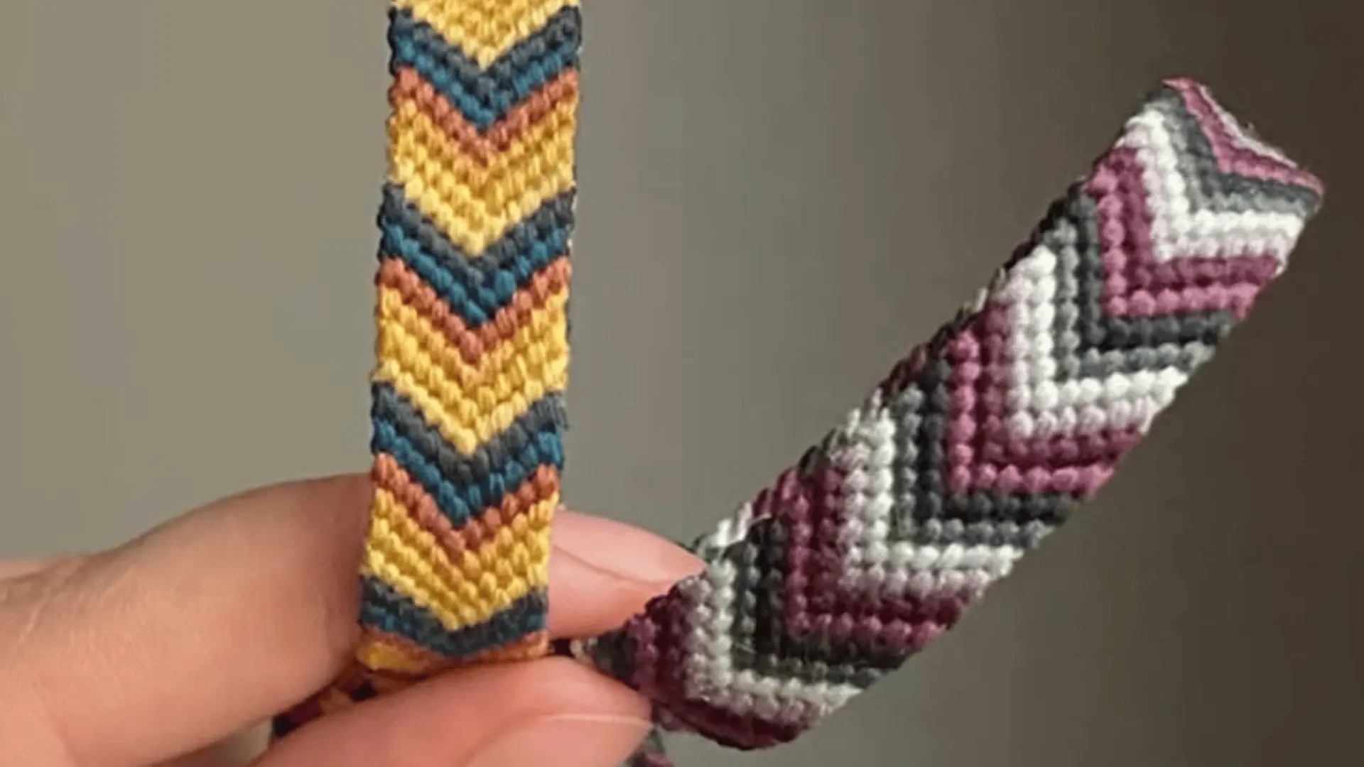 Two woven friendship bracelets with V-shape bold chevron patterns being held up by a hand.