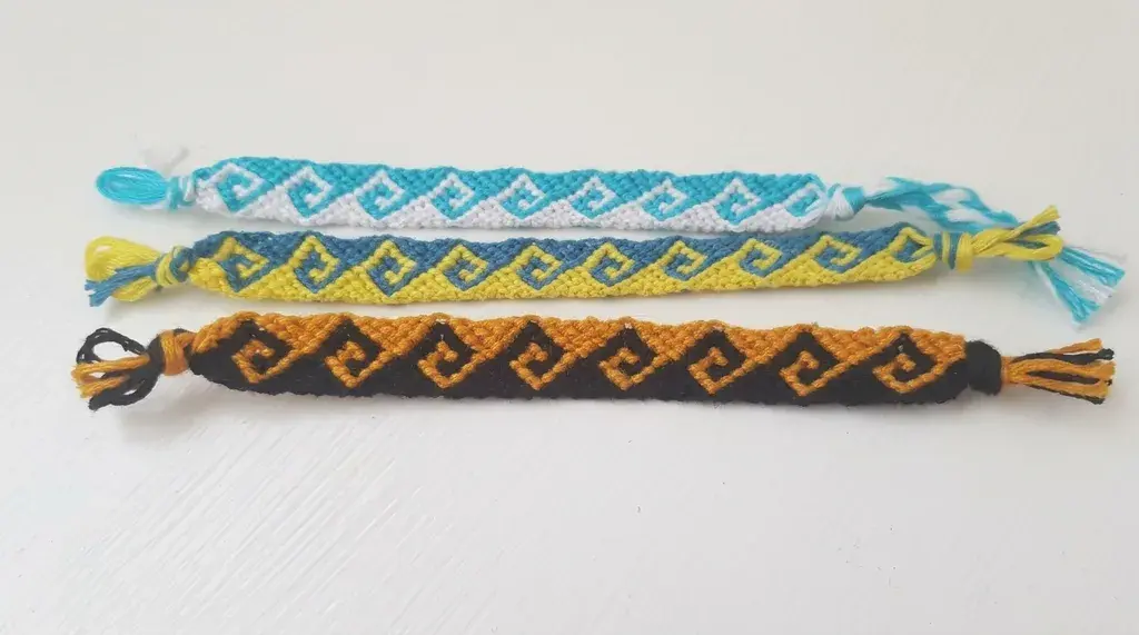 Three woven friendship bracelets with Greek key / wave patterns in blue/white, yellow/blue, and orange/black.