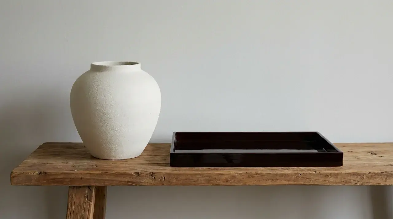 Matte ceramic vase beside lacquered tray on raw wood surface showing contrast in finish types